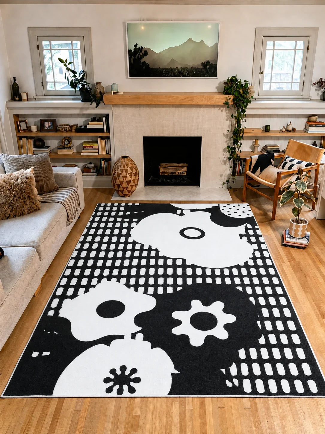 7' × 10' Black and White Abstract Floral Rug by Becca Franks with oversized white flowers and grid marks between a gray sofa and wooden armchair.