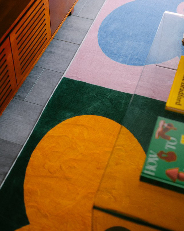 Close-up of colorful clover rug under a glass table, featuring yellow and blue clovers on green and pink backgrounds.