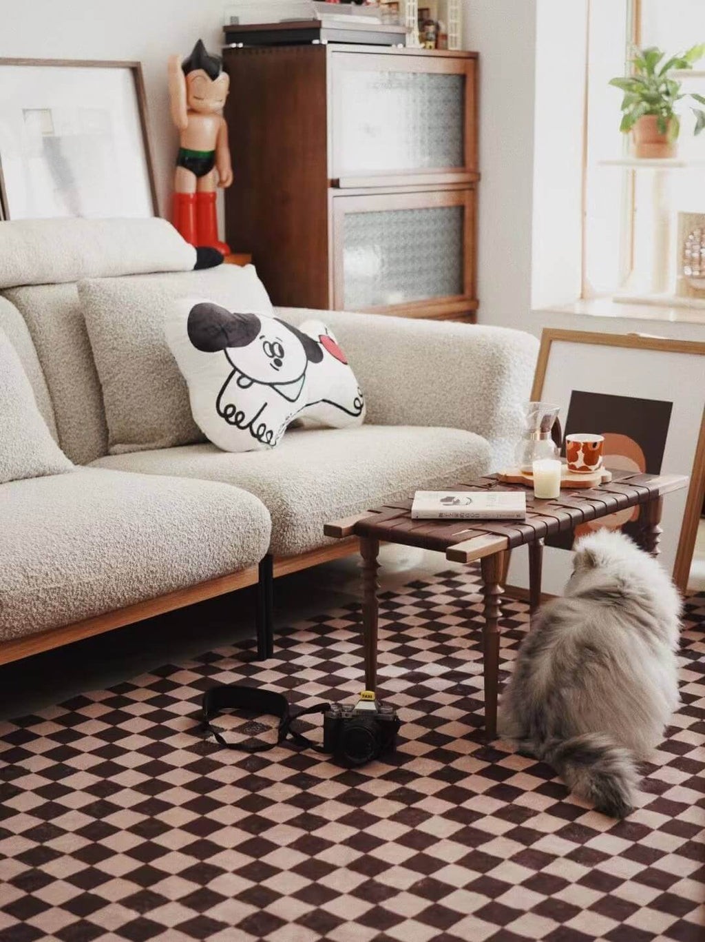 A fluffy cat lounges next to a mid-century sofa on the checkered rug, creating a playful and lived-in modern interior.
