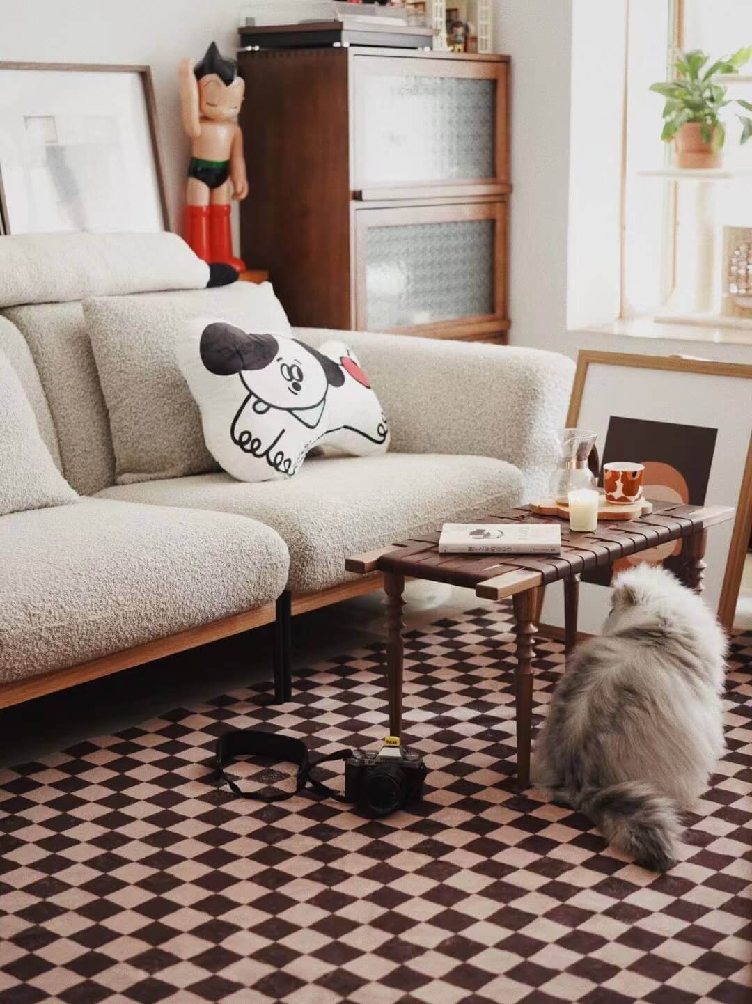 A fluffy cat lounges next to a mid-century sofa on the checkered rug, creating a playful and lived-in modern interior.