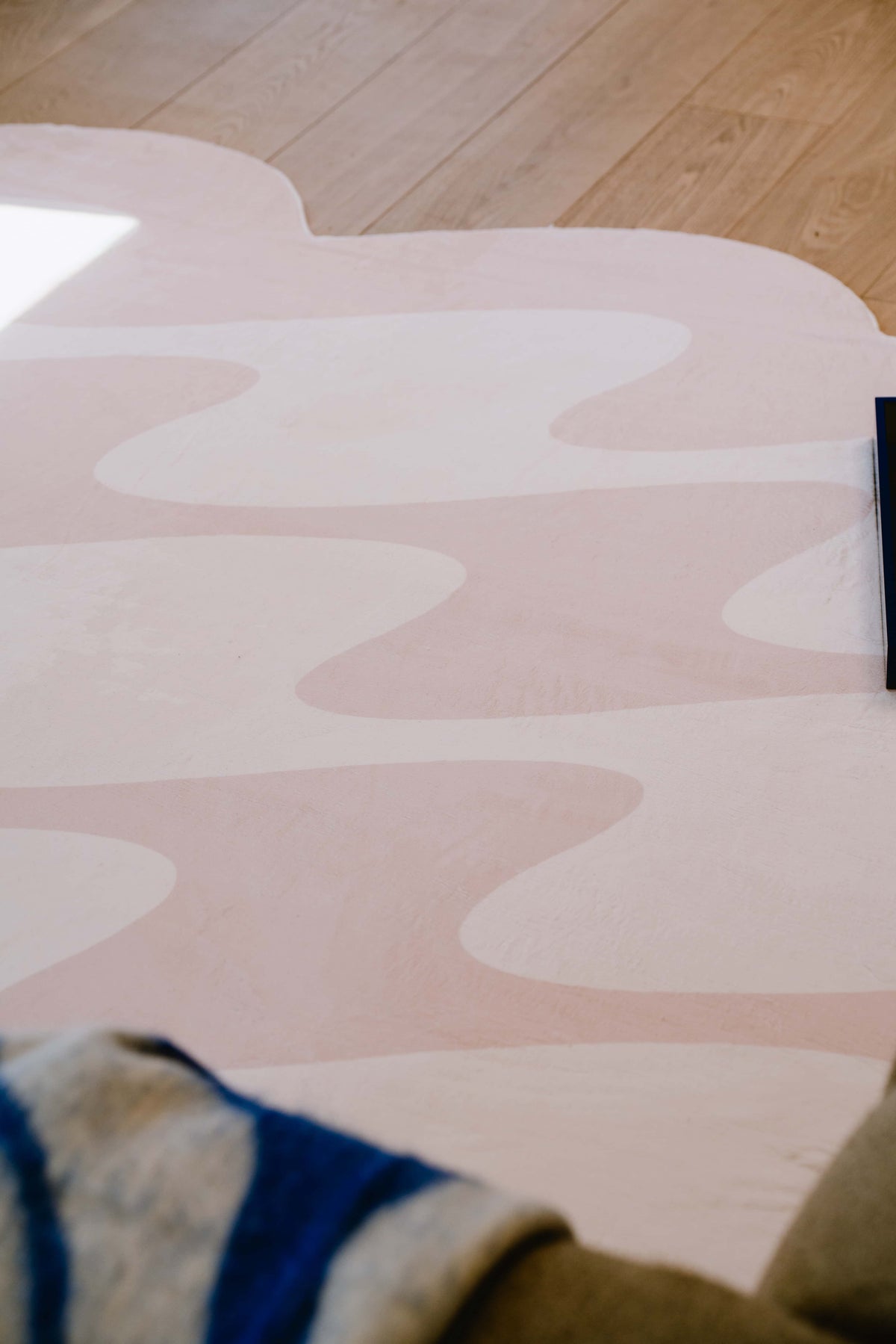 Playful pastel pink wavy rug with curved edges brings warmth and charm to a sunlit living space with light wood floor.