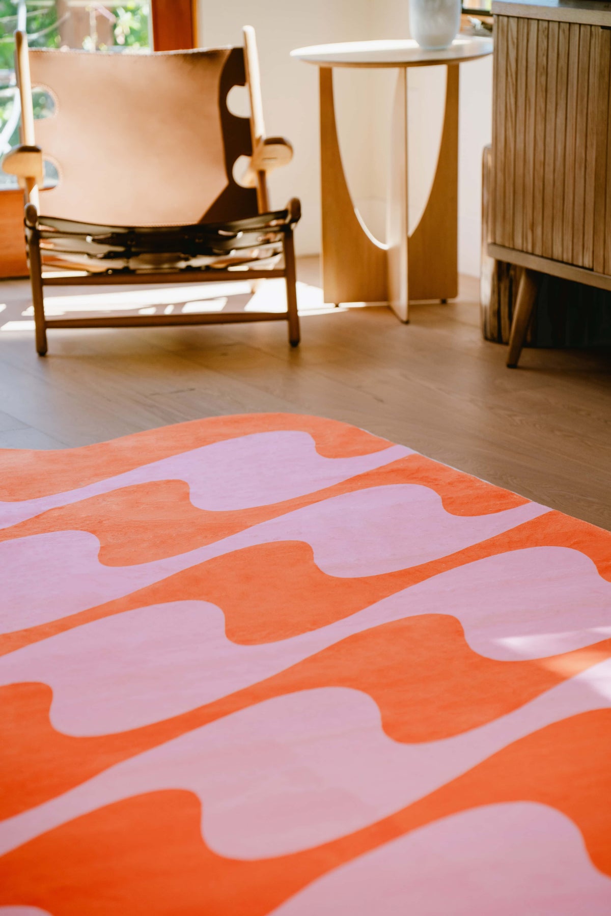 Close-up of pastel irregular shaped wavy rug in orange and pink, placed near wooden chair.