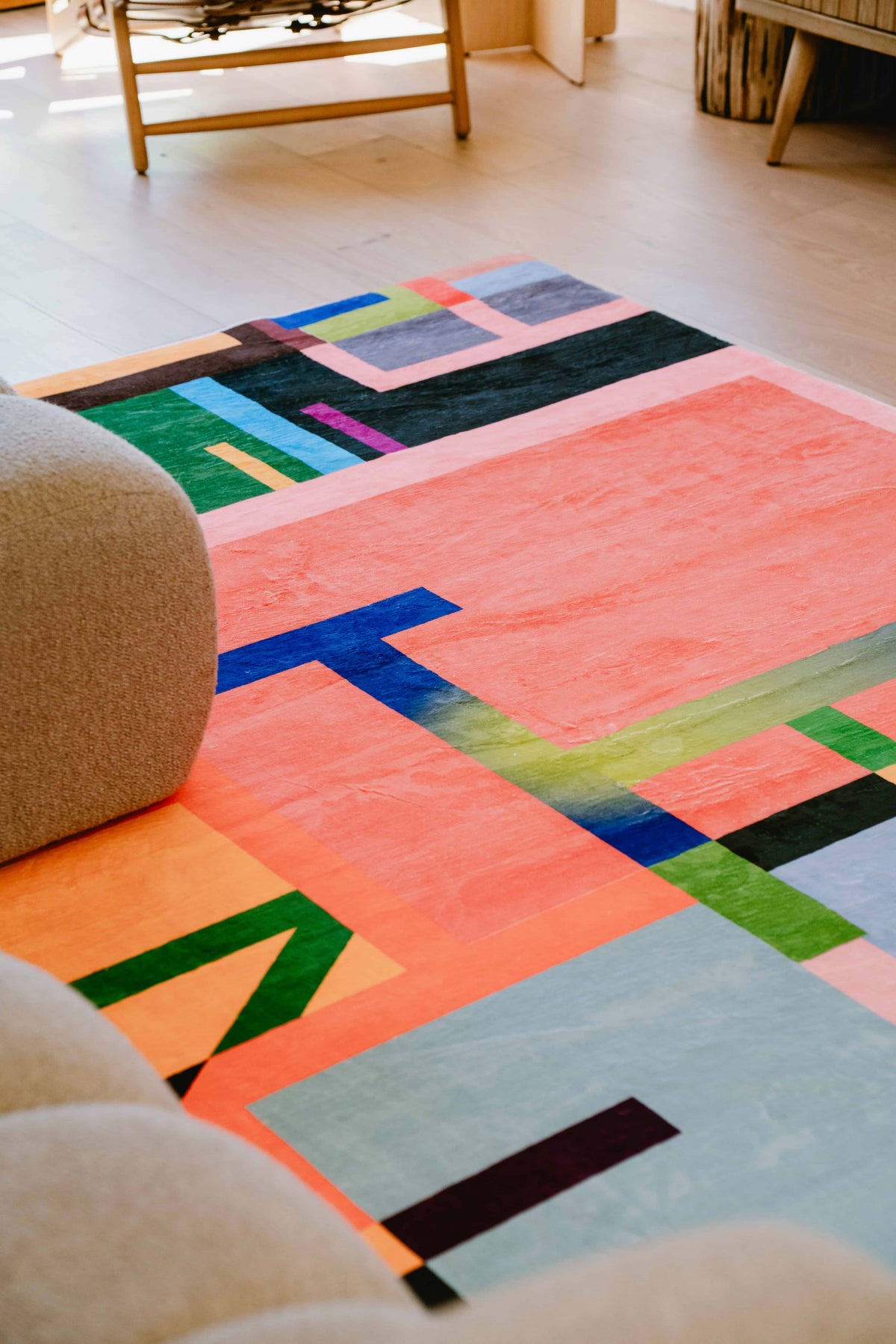 Colorful geometric rug with bold blocks beside beige sofa, creating a vibrant focal point in a cozy living space.