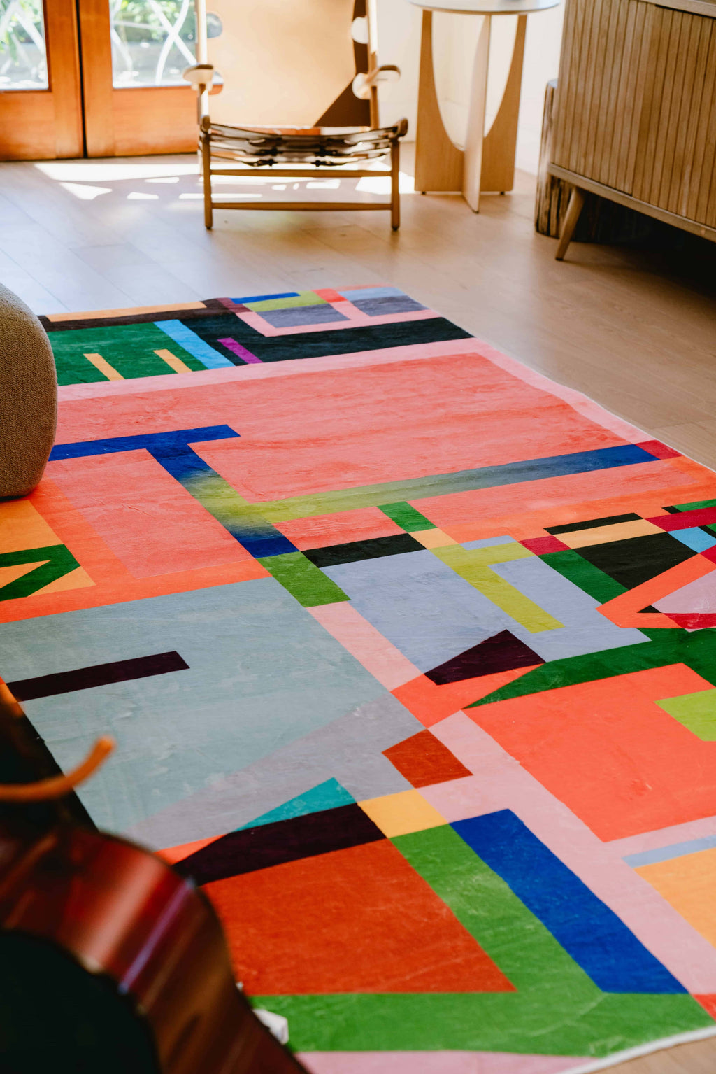Multicolored block abstract area rug in living room with natural light, wood floors, and mid-century modern decor.