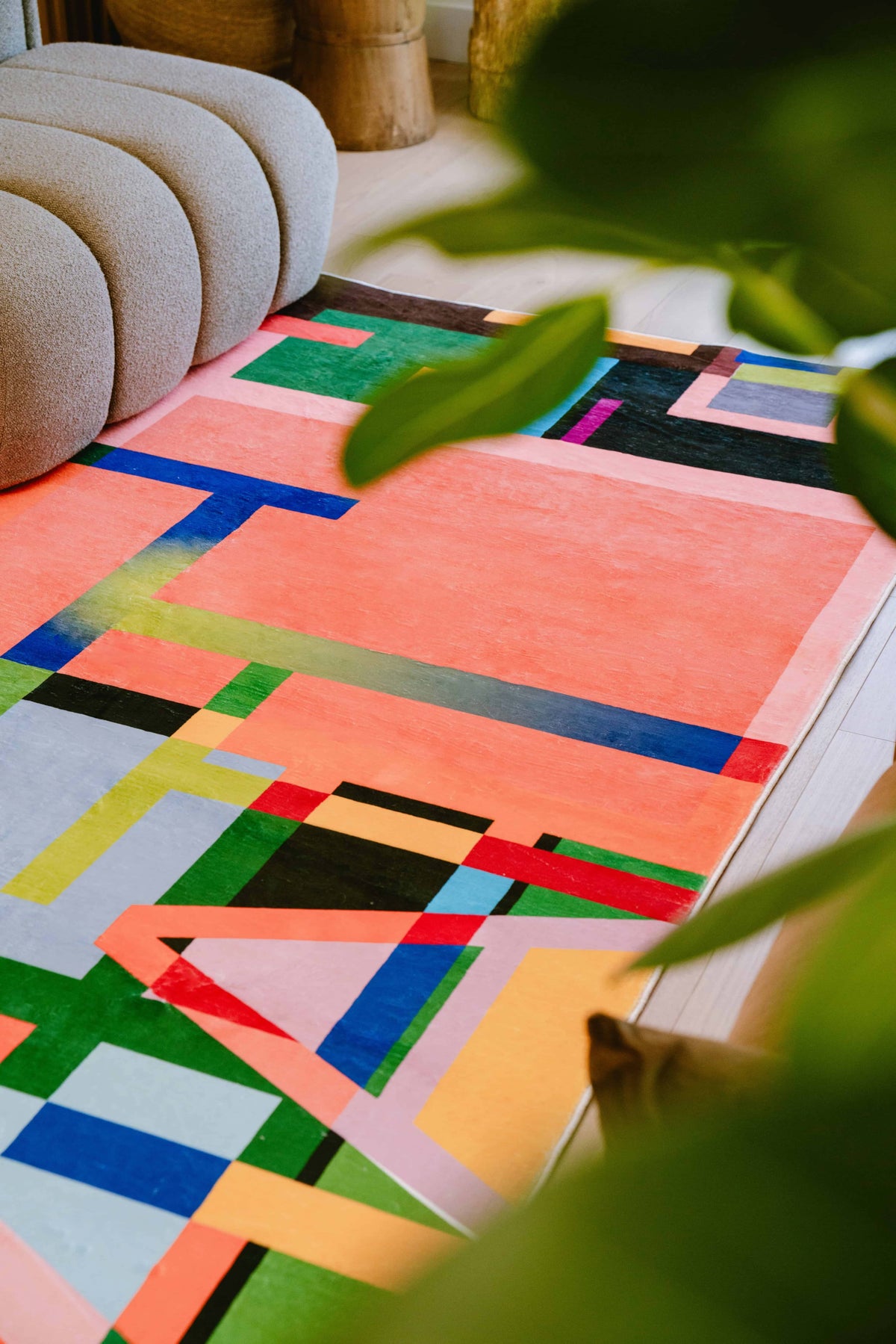 Angled view of multicolored block rug under sofa with greenery partially obscuring the frame.