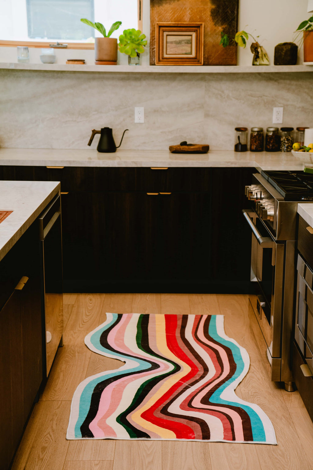Wavy multicolor contour rug in modern kitchen interior, placed between dark cabinets and a silver stove.