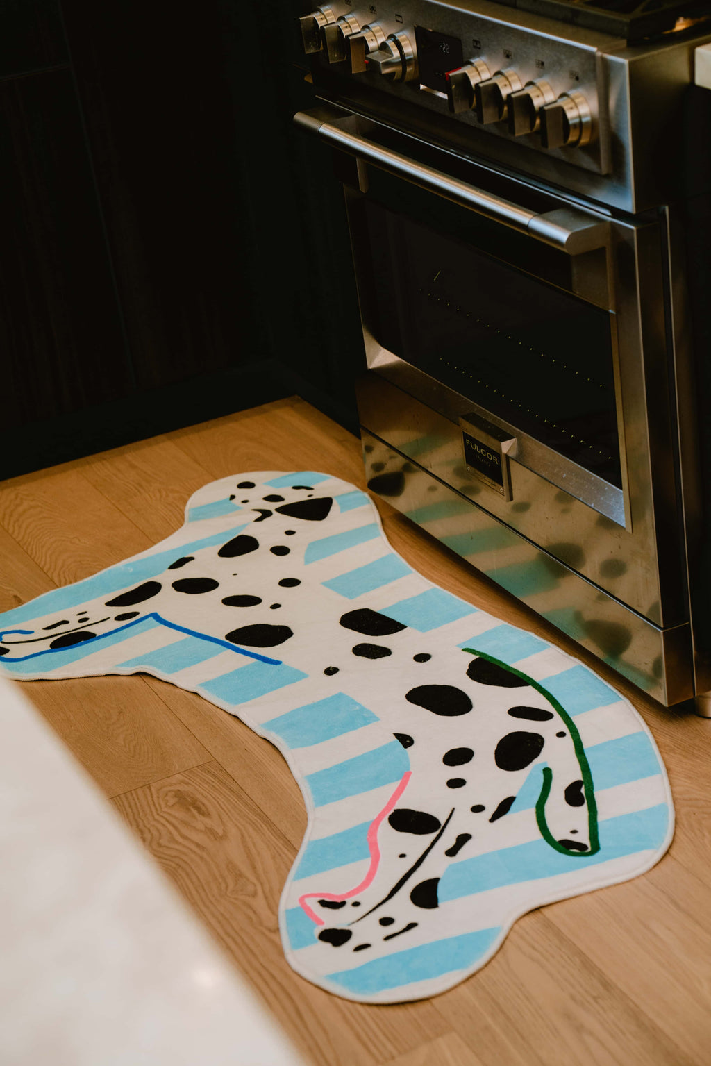 Irregular dog-shaped runner rug laid across the kitchen floor near the oven and dark wood cabinets.