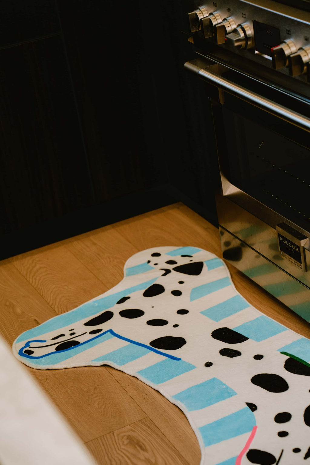 Close-up of dog-shaped runner rug placed in front of a stainless steel oven on light wood floor.