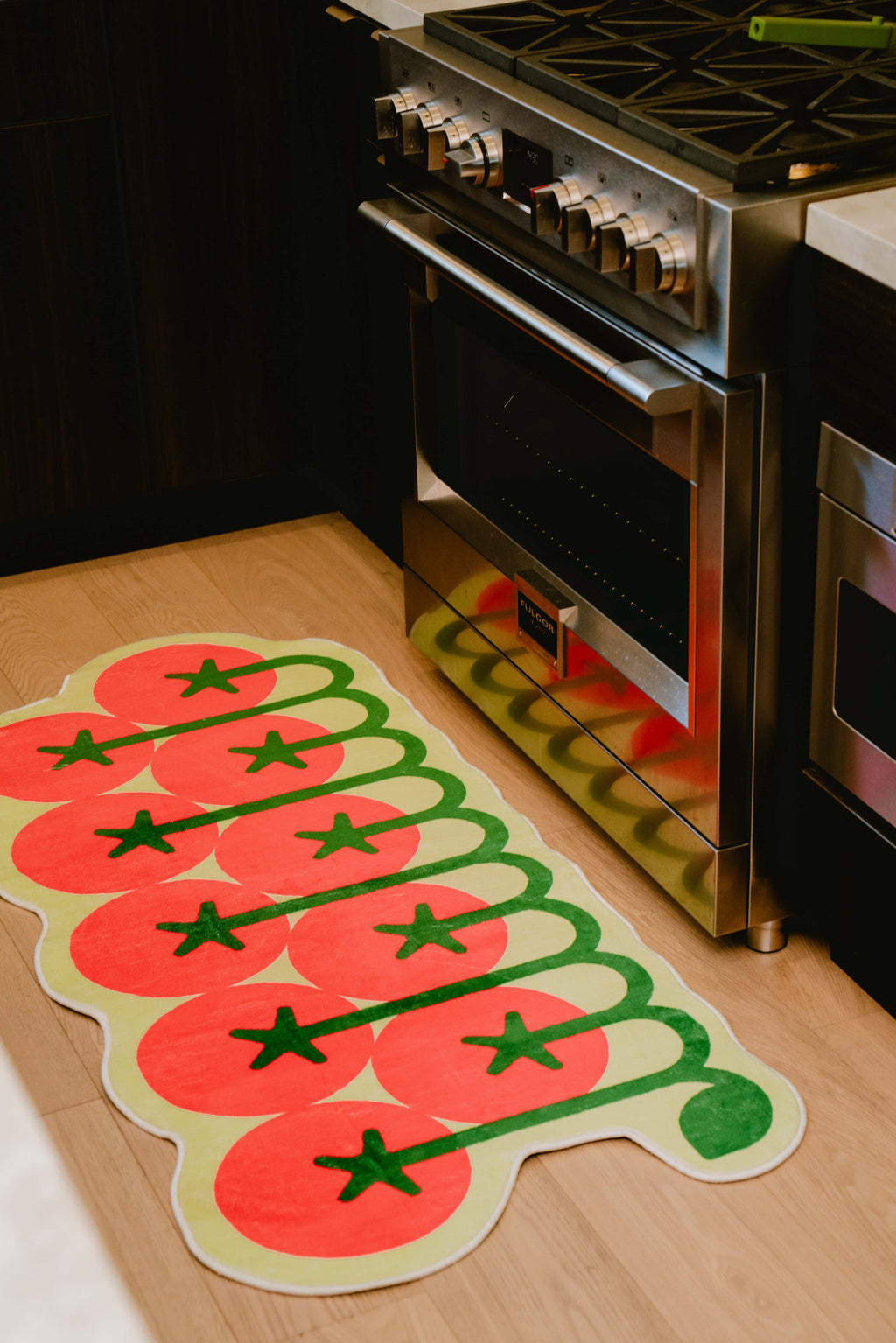 Tomato rug adds a playful touch beneath the stove, creating a bold accent against the dark cabinetry in the kitchen.