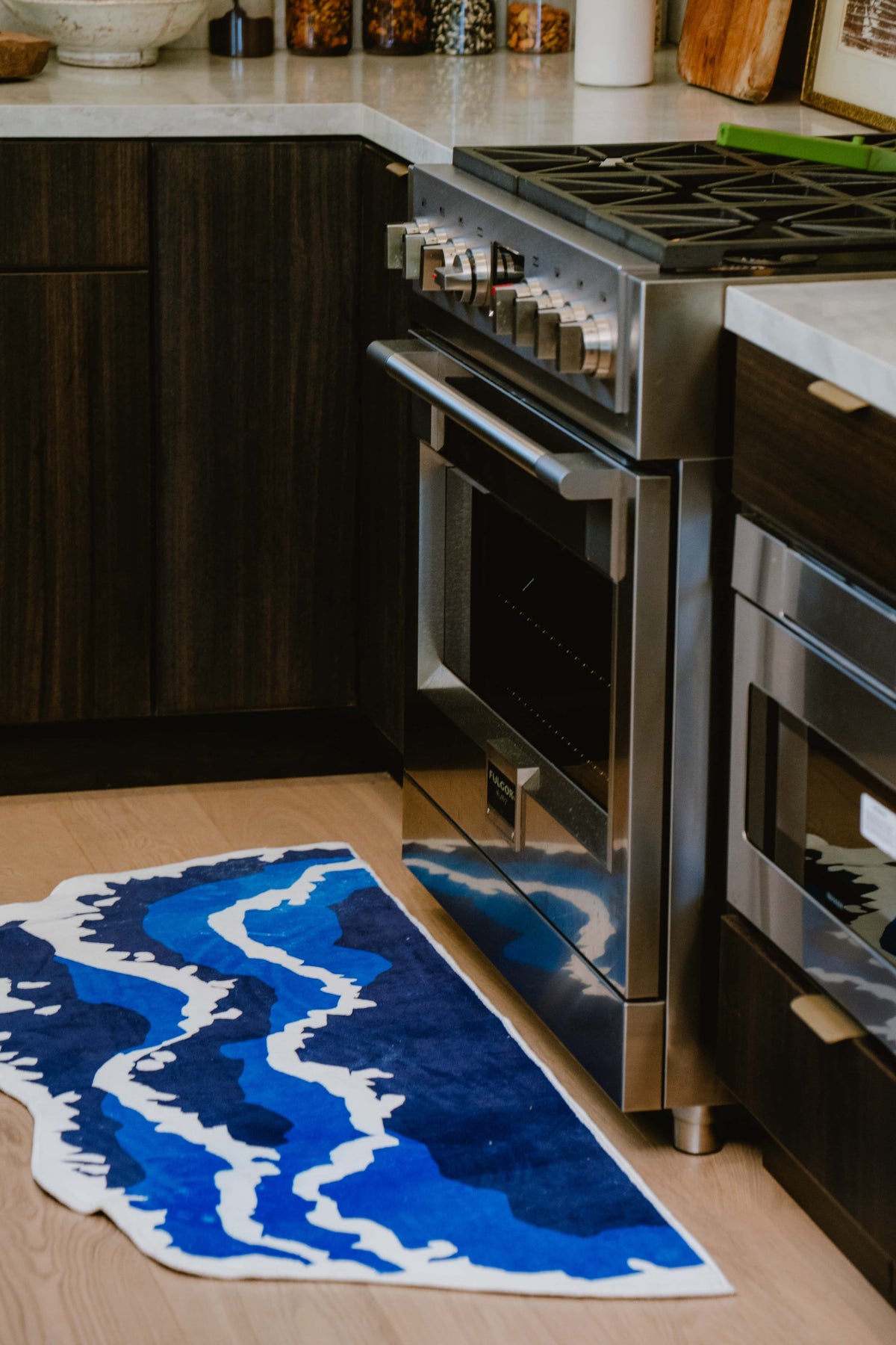 Multicolor kitchen scene featuring an irregular blue wavy runner rug placed by the stove on light wooden floor.