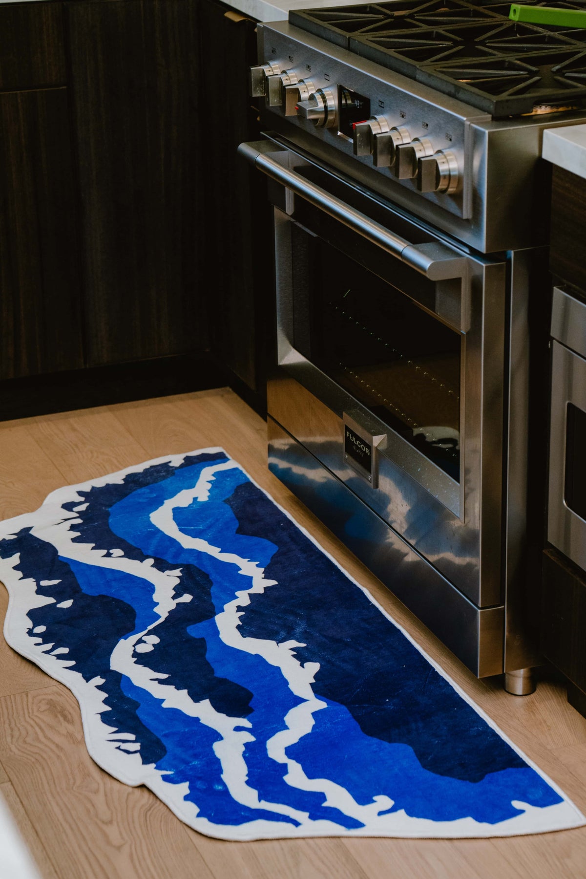 Closer look at the irregular blue wavy runner rug laid near a stainless steel oven on a light-toned kitchen floor.