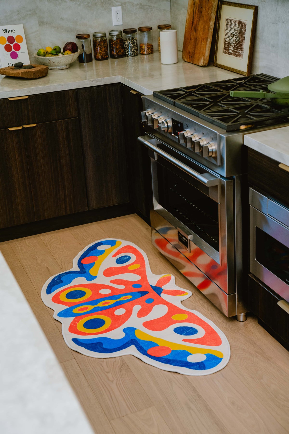 Butterfly rug on light wood flooring in front of a modern stove and dark wood cabinetry, under warm lighting.