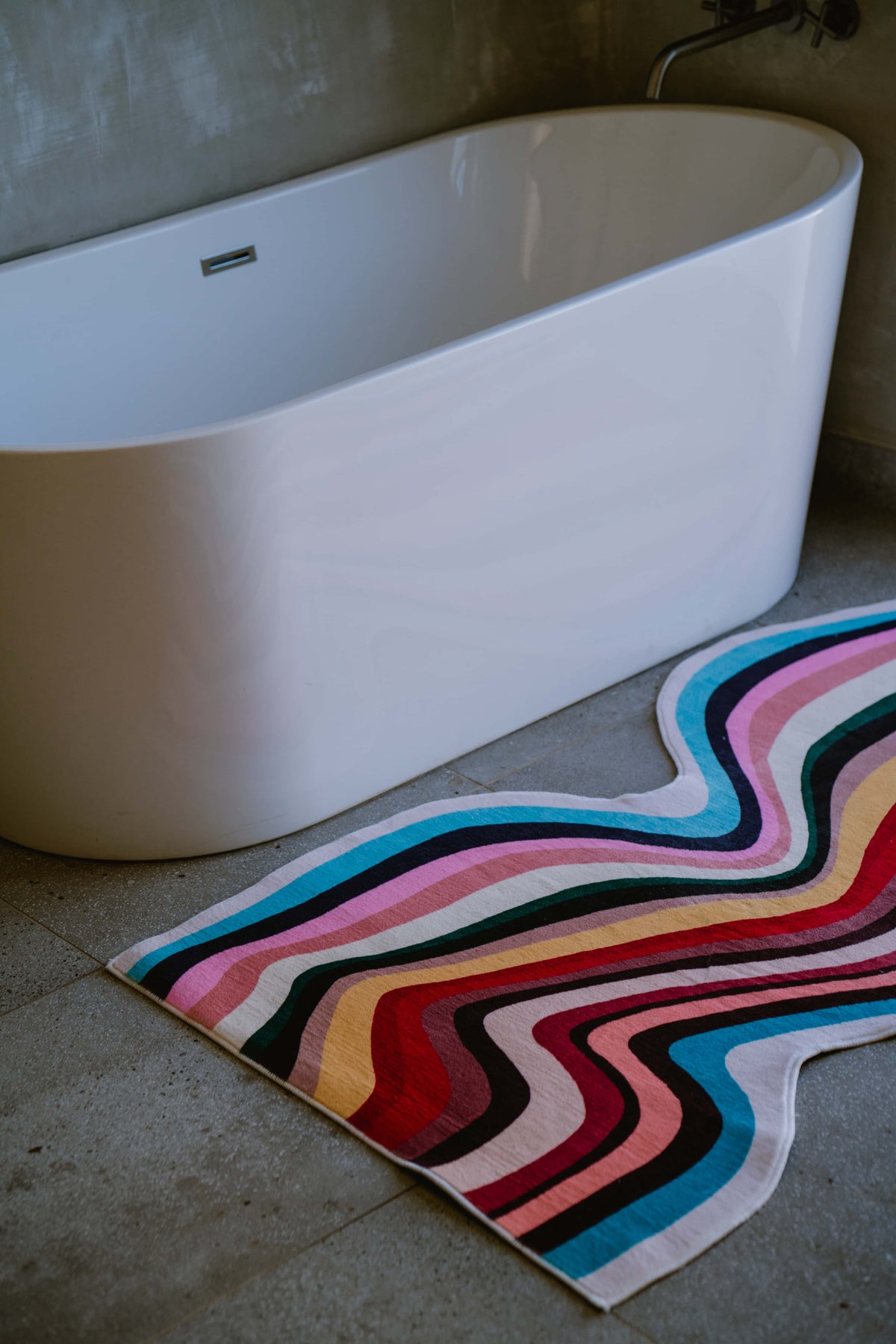 Close-up of the colorful striped contour runner rug with curvy edges, styled next to a freestanding bathtub.