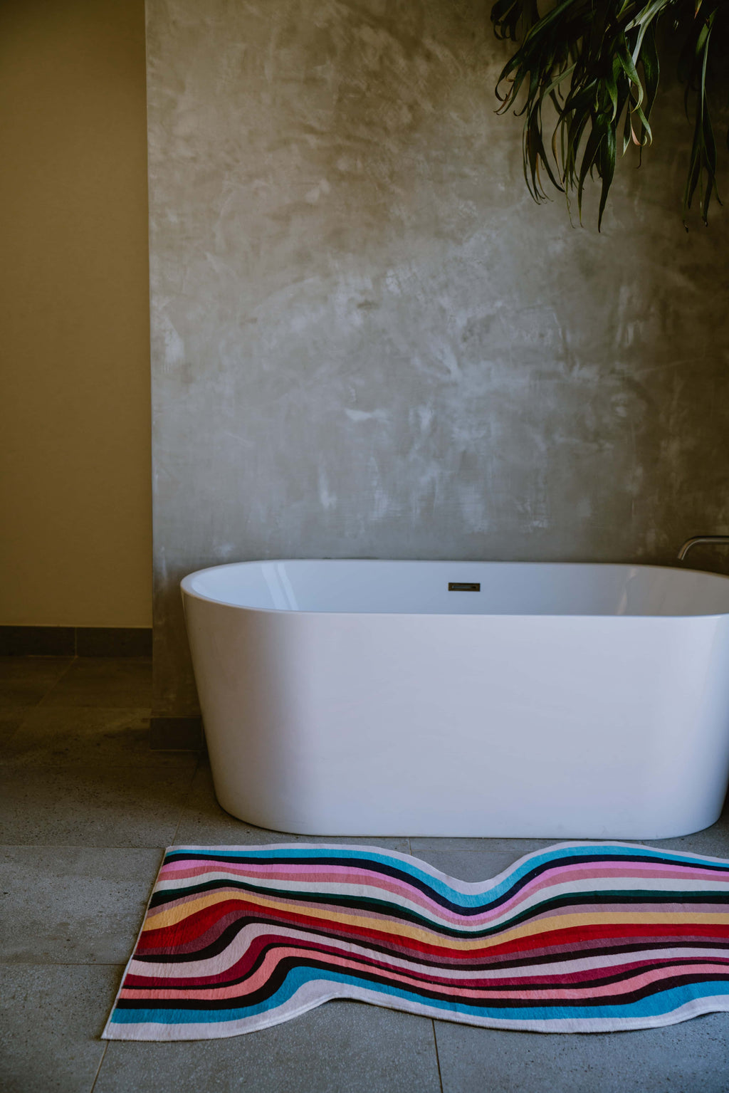 Wavy multicolor contour runner rug placed beside a modern white tub in a warm-toned minimalist bathroom.