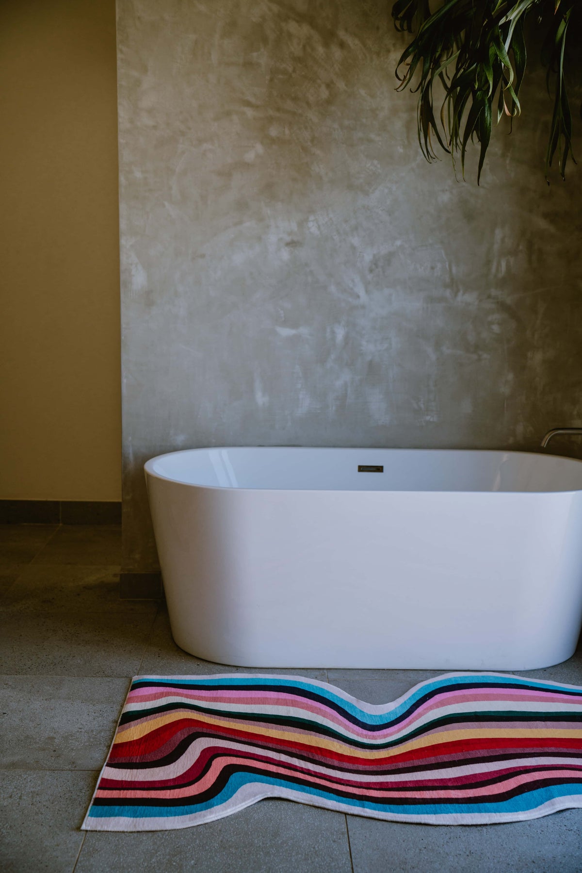 Wavy multicolor contour runner rug placed beside a modern white tub in a warm-toned minimalist bathroom.