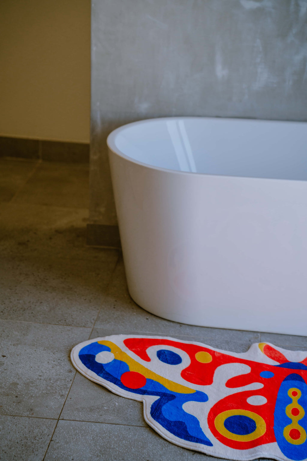 Partial view of butterfly rug on stone tiles next to a curved tub, in a minimalist corner with soft shadows.