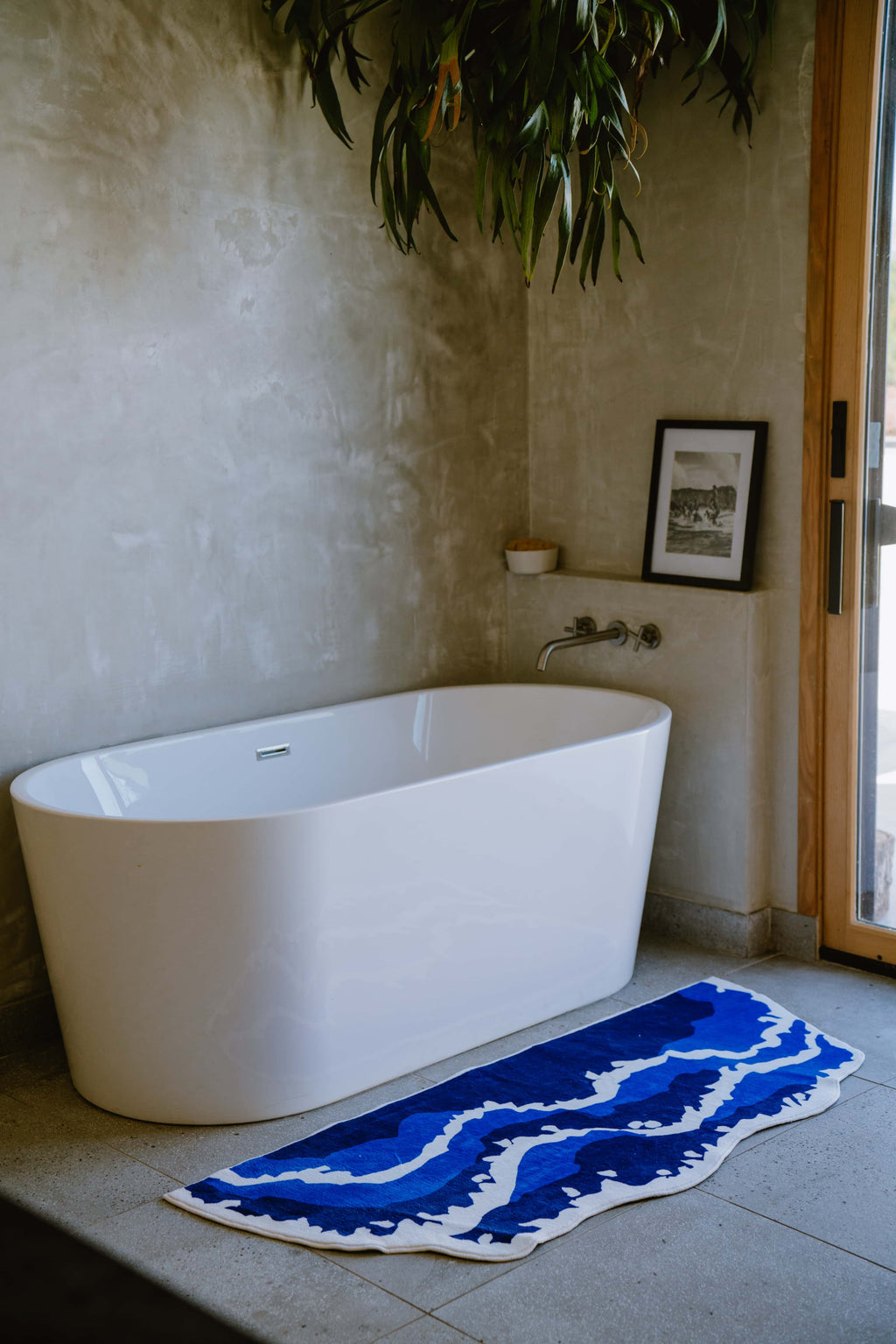 Irregular Shaped Blue Wavy Runner Rug beside a freestanding bathtub in a serene, concrete-walled bathroom with natural light.