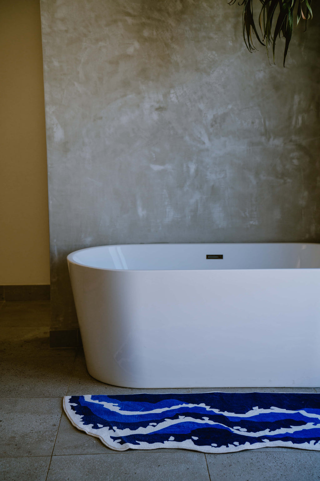 Blue wavy runner rug placed neatly by the tub, bringing bold color and shape contrast to a modern stone-tiled bathroom.