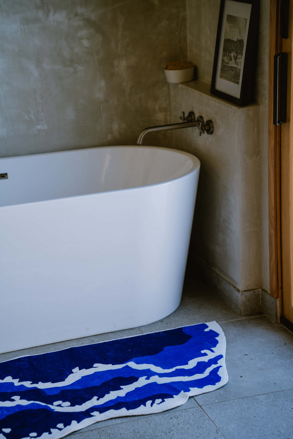 Close-up of the blue wavy rug showing texture and playful shape on bathroom floor next to a minimalist white soaking tub.