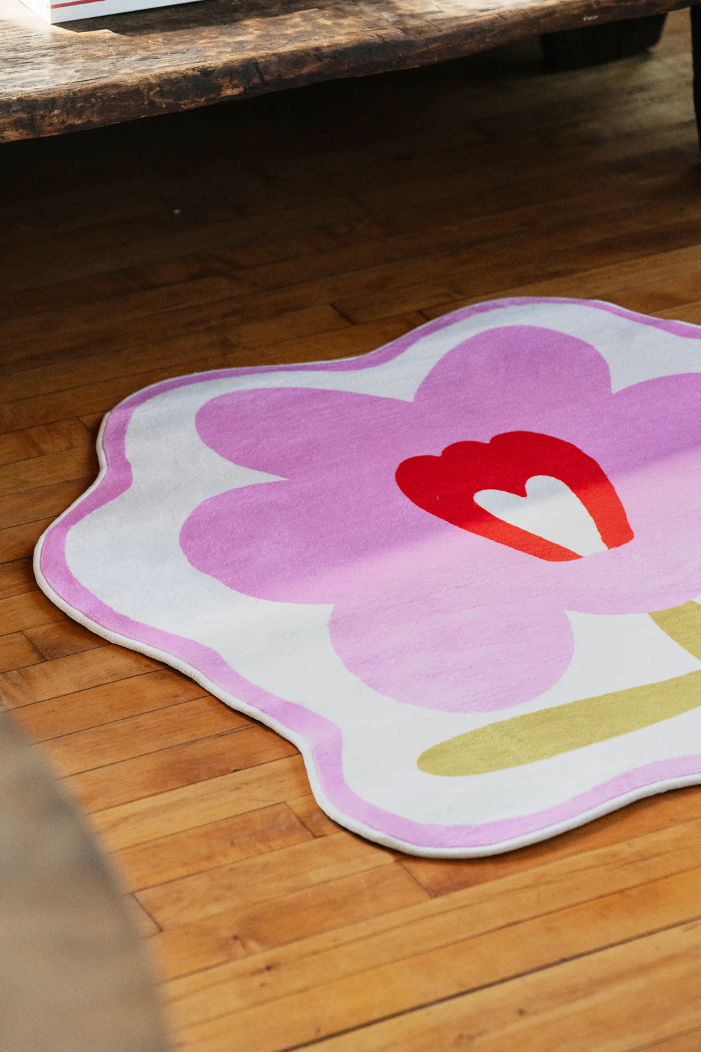Modern area rug in bold orange flower shape placed on polished floor, catching soft afternoon sun near a chair.