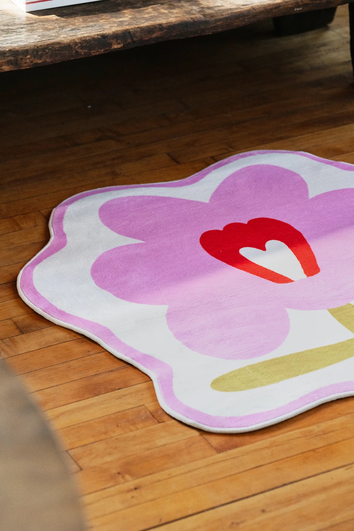 Modern area rug in bold orange flower shape placed on polished floor, catching soft afternoon sun near a chair.