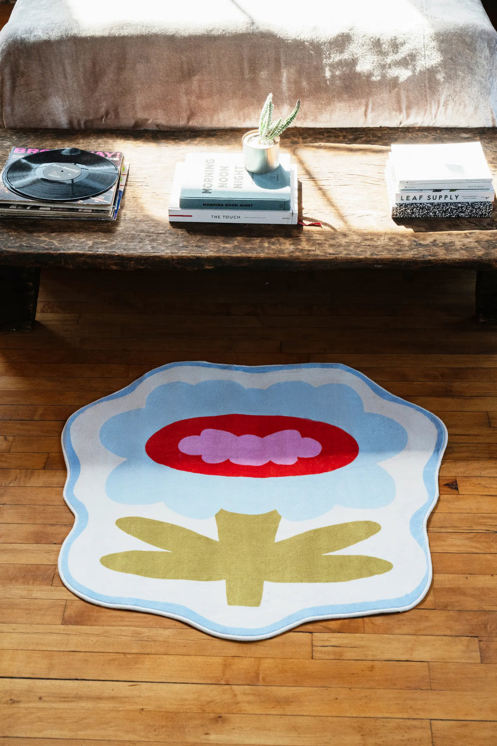 Modern area rug in bold blue flower shape placed beneath cozy table corner, adding charm to sunlit wood floor.