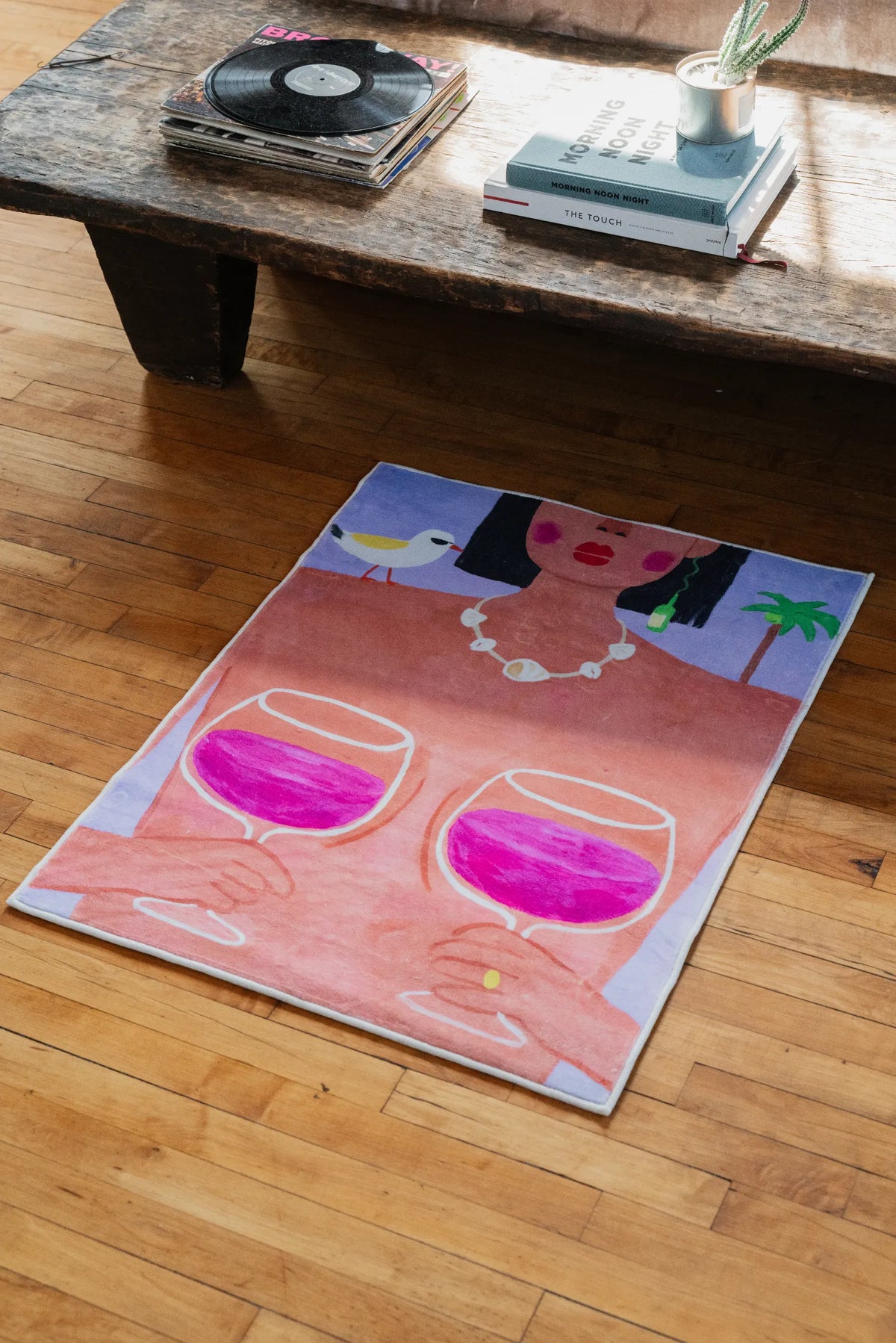 Funky art rug showing bold wine glasses and woman face laid on polished wood floor beside vintage record player stand.