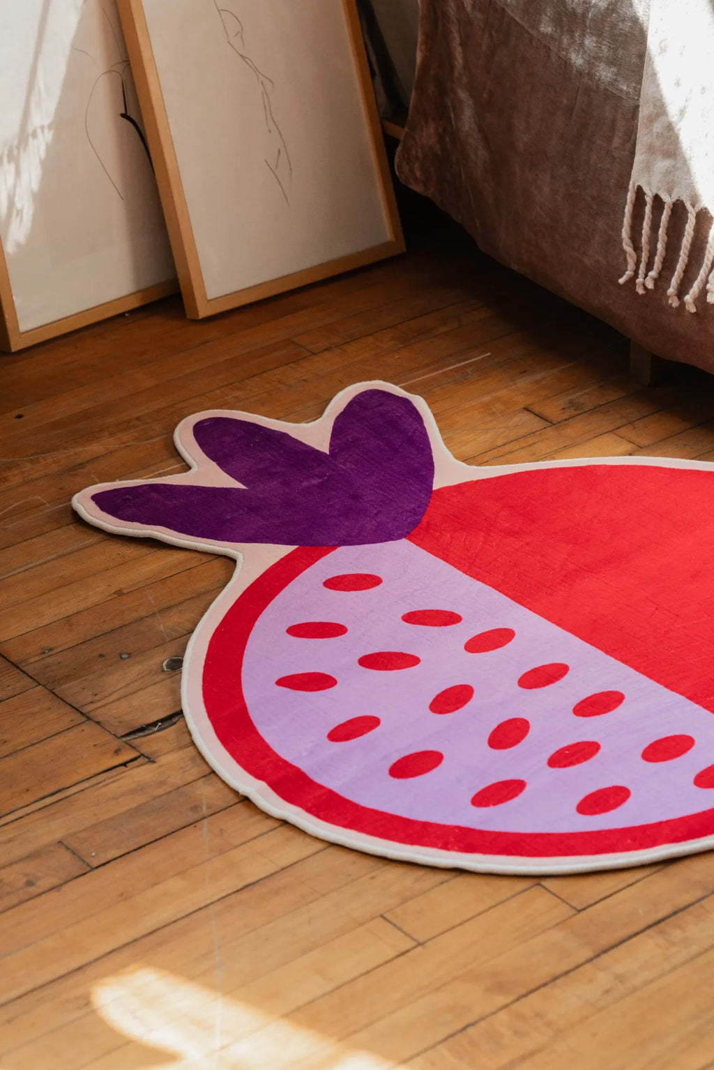 Close-up of the pomegranate rug showing its vivid red surface and purple crown detail on a natural wood floor.