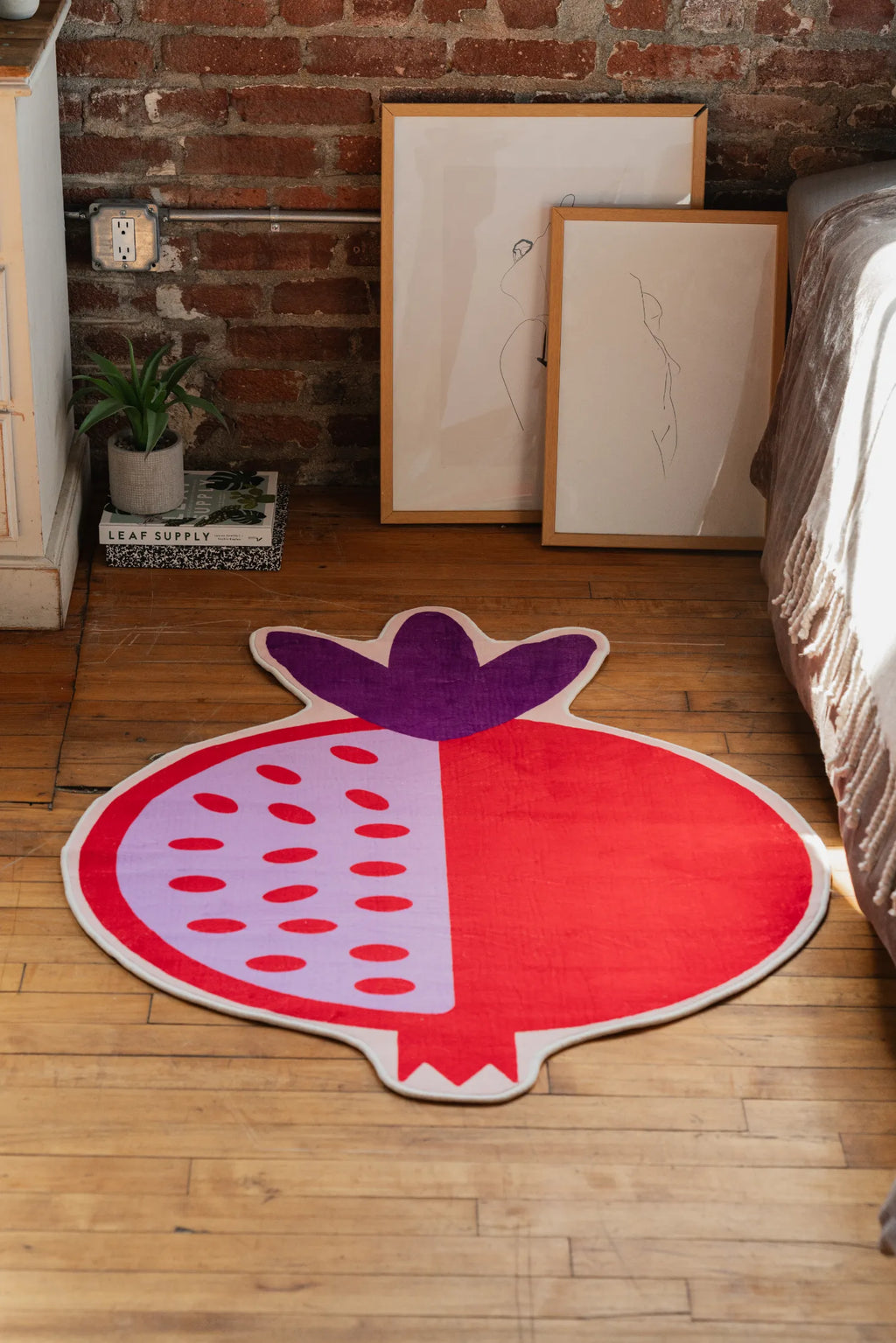 Red Pomegranate Shaped Irregular Rug by Shayla Goethe styled in bedroom with framed art and sunlight on floor.