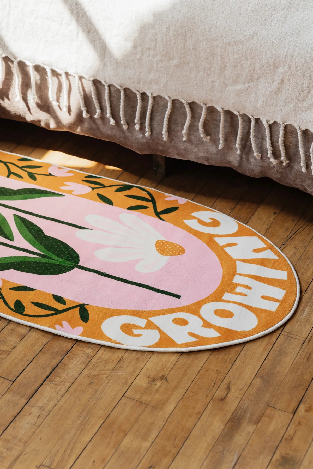 Playful rug with daisy quote design lying partly under the edge of a bed on warm wood floor in a bright bedroom.
