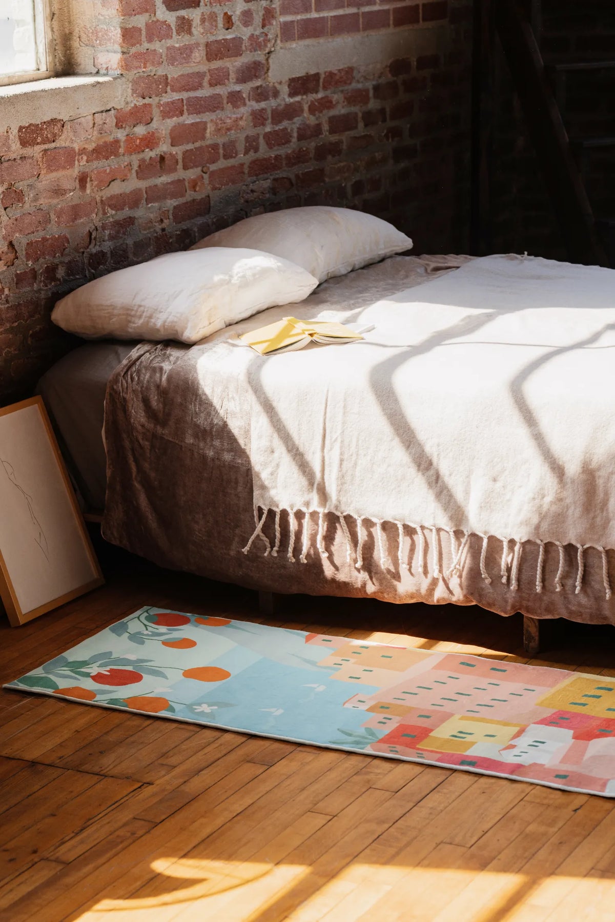 Bed with white bedding in a room with brick walls and a colorful rug on the floor.