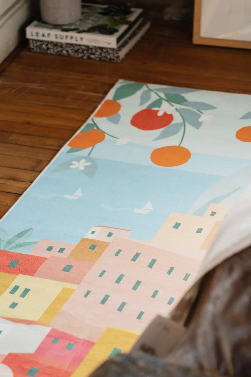 Decorative runner with Italian village and fruit design resting on a wooden floor near books