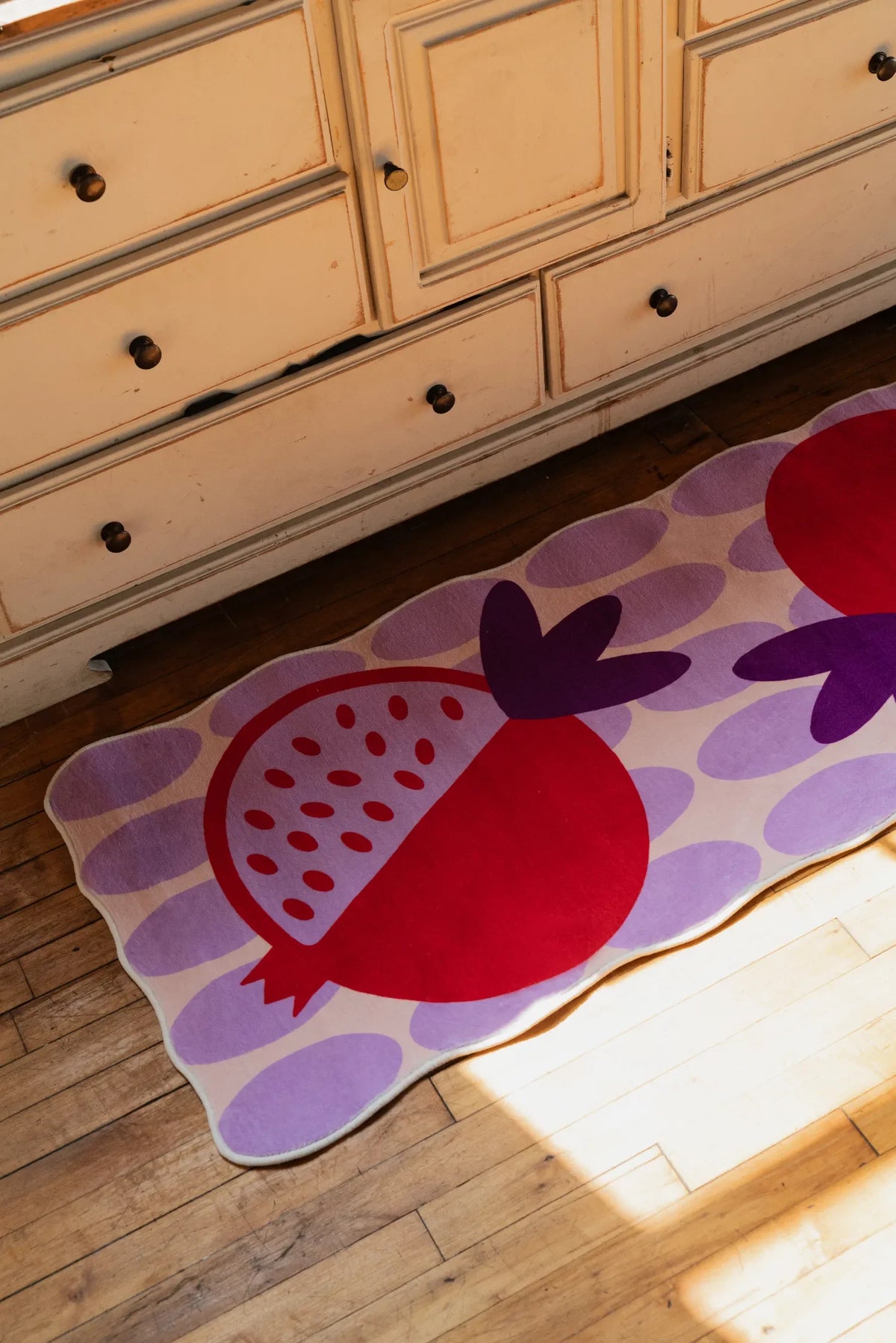 Colorful fruit-themed rug with bold pomegranate shapes, brightening a cozy bedroom corner with vintage furniture.