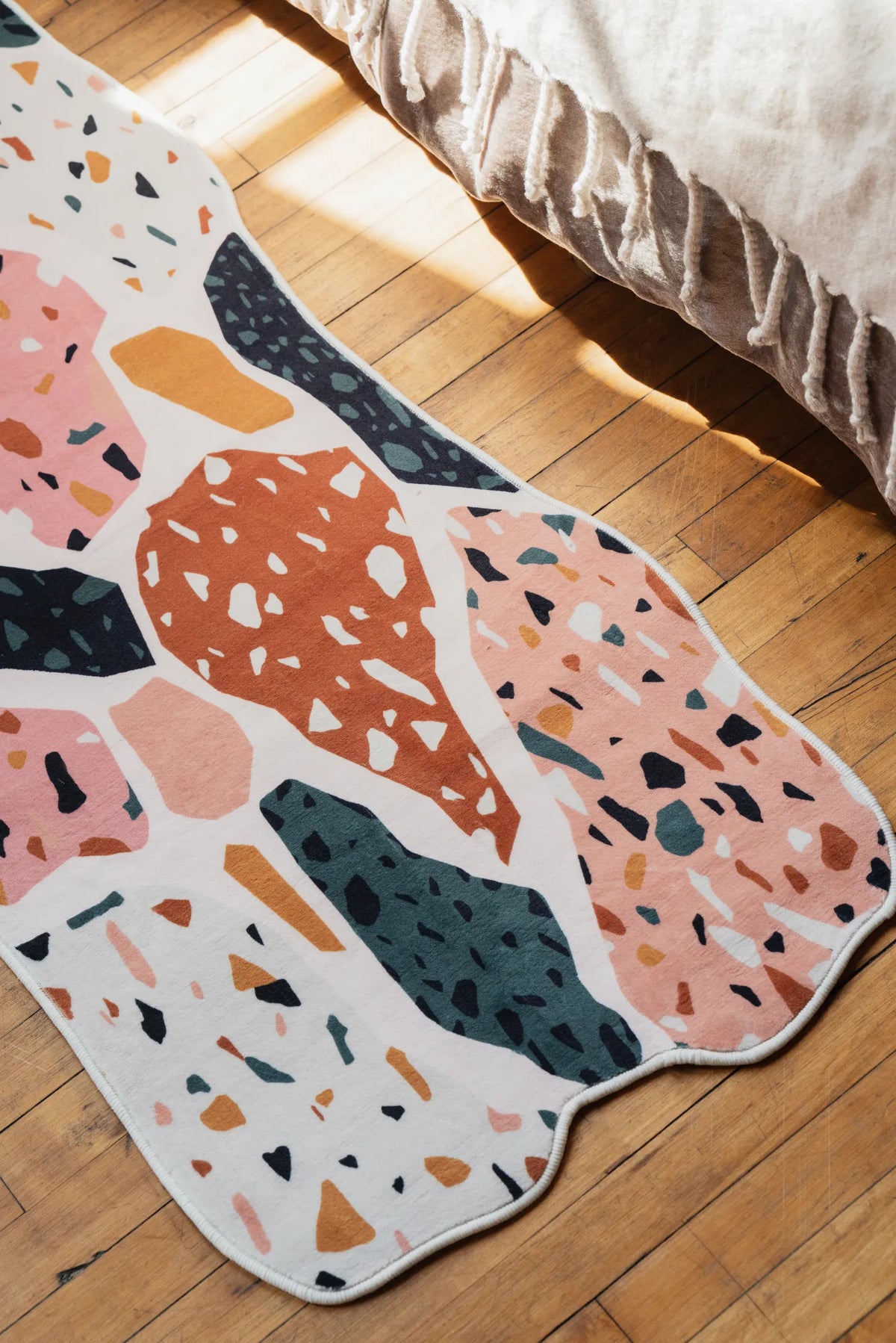 A colorful abstract runner rug with mosaic patterns styled on warm wood floor beside the bed.