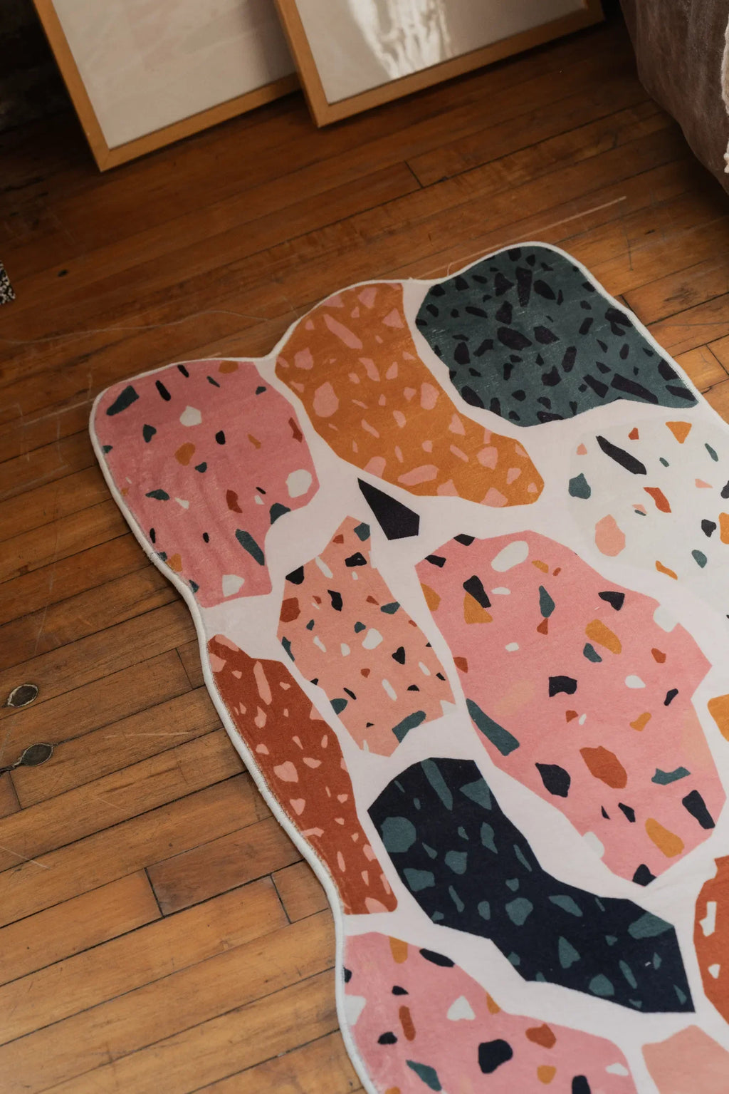 Close-up of an abstract runner rug on wood floor, showcasing its mosaic patterns in pink, orange, and dark tones.