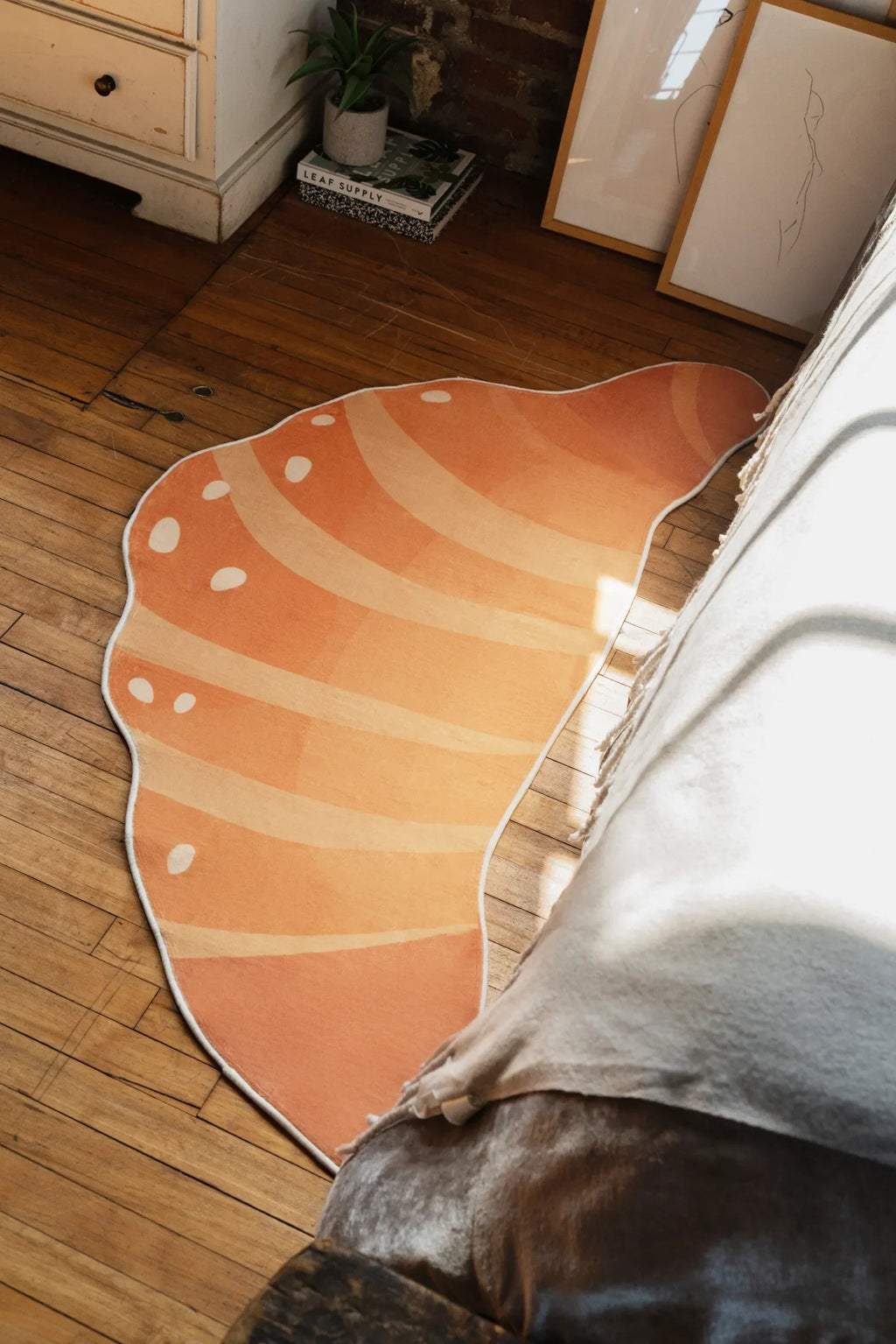 Buttery orange croissant rug lying near framed art pieces on a wood floor with soft shadows