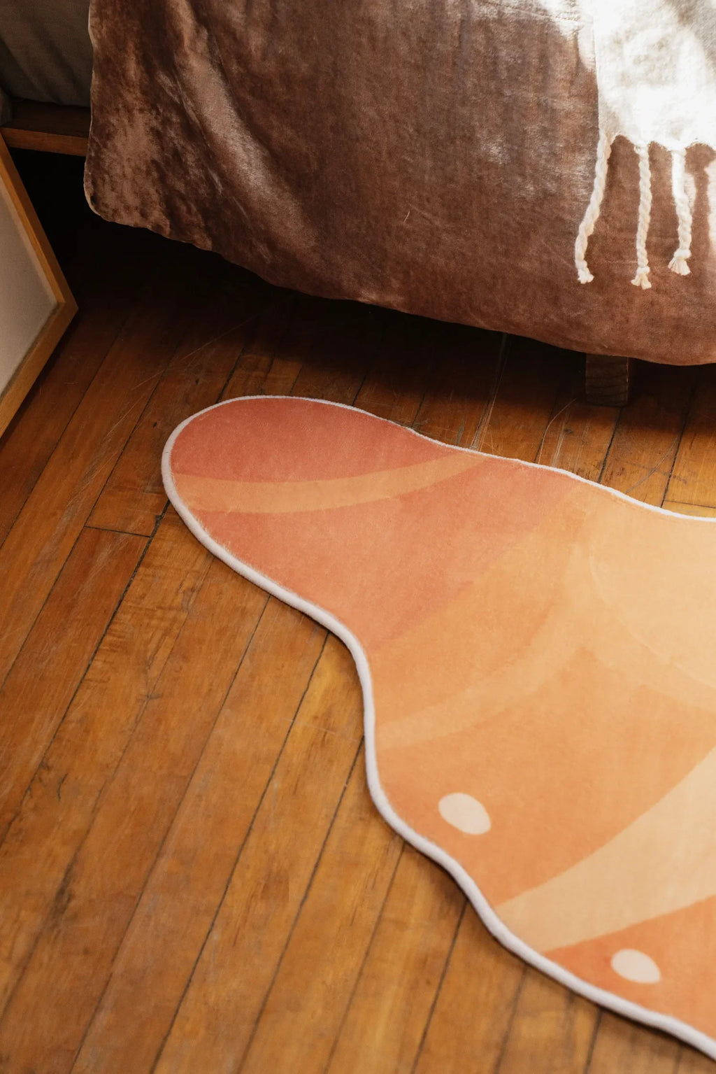 Playful croissant rug in warm orange tones tucked beside a brown blanket on wooden floor