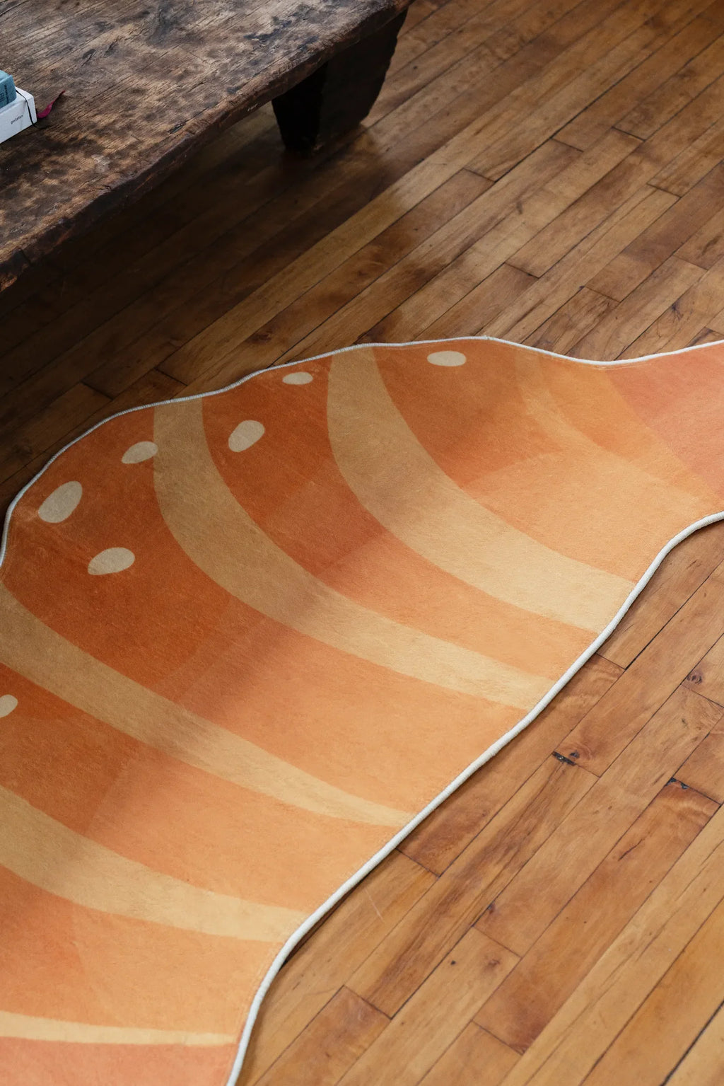 Croissant-shaped rug stretched across a wood floor near a rustic bench, highlighting its warm orange tones and curved edges