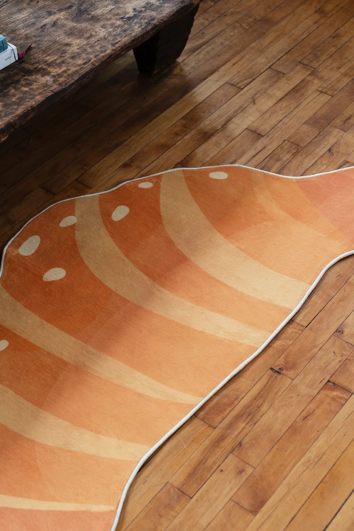Croissant-shaped rug stretched across a wood floor near a rustic bench, highlighting its warm orange tones and curved edges