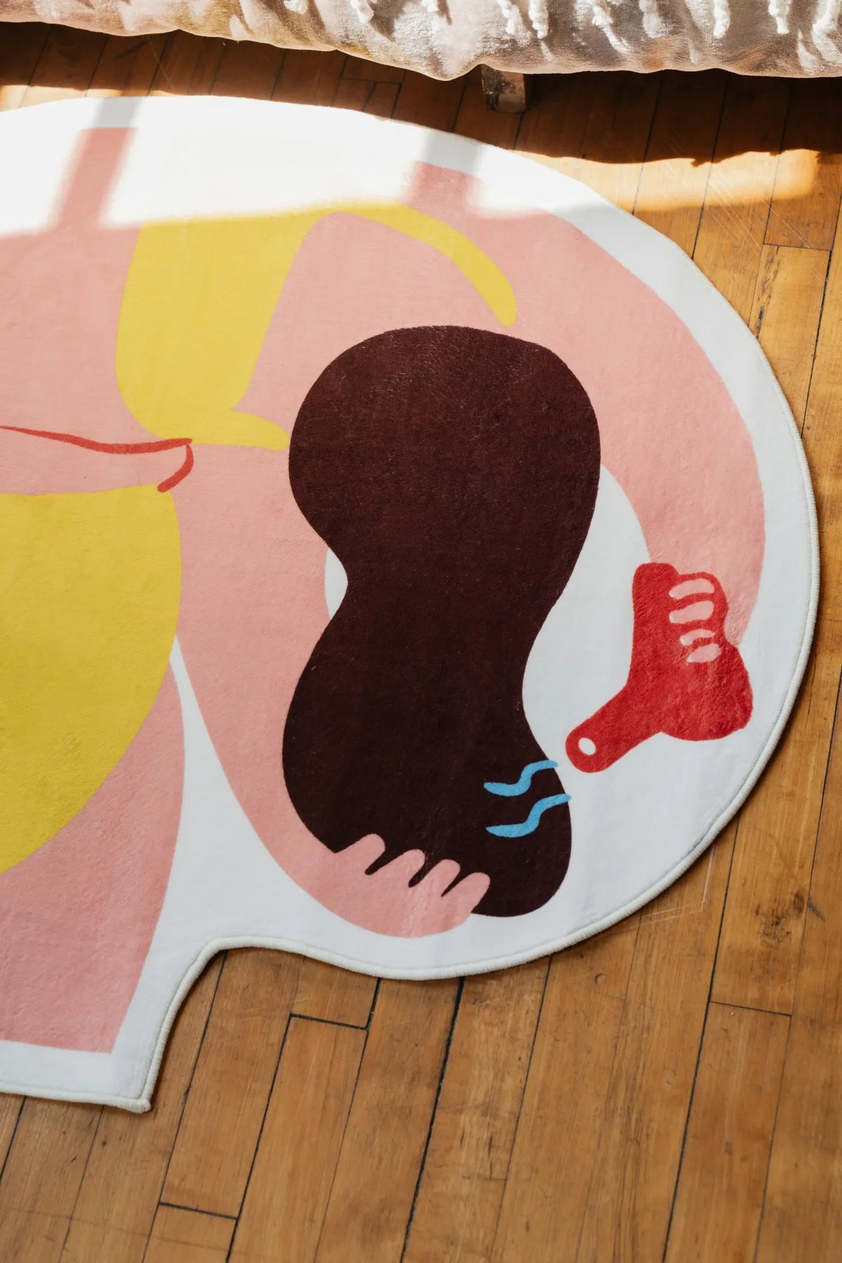 Close-up of Funky Body Art Rug by Nimei in pink, yellow, and brown tones, sunlight across wooden floor.