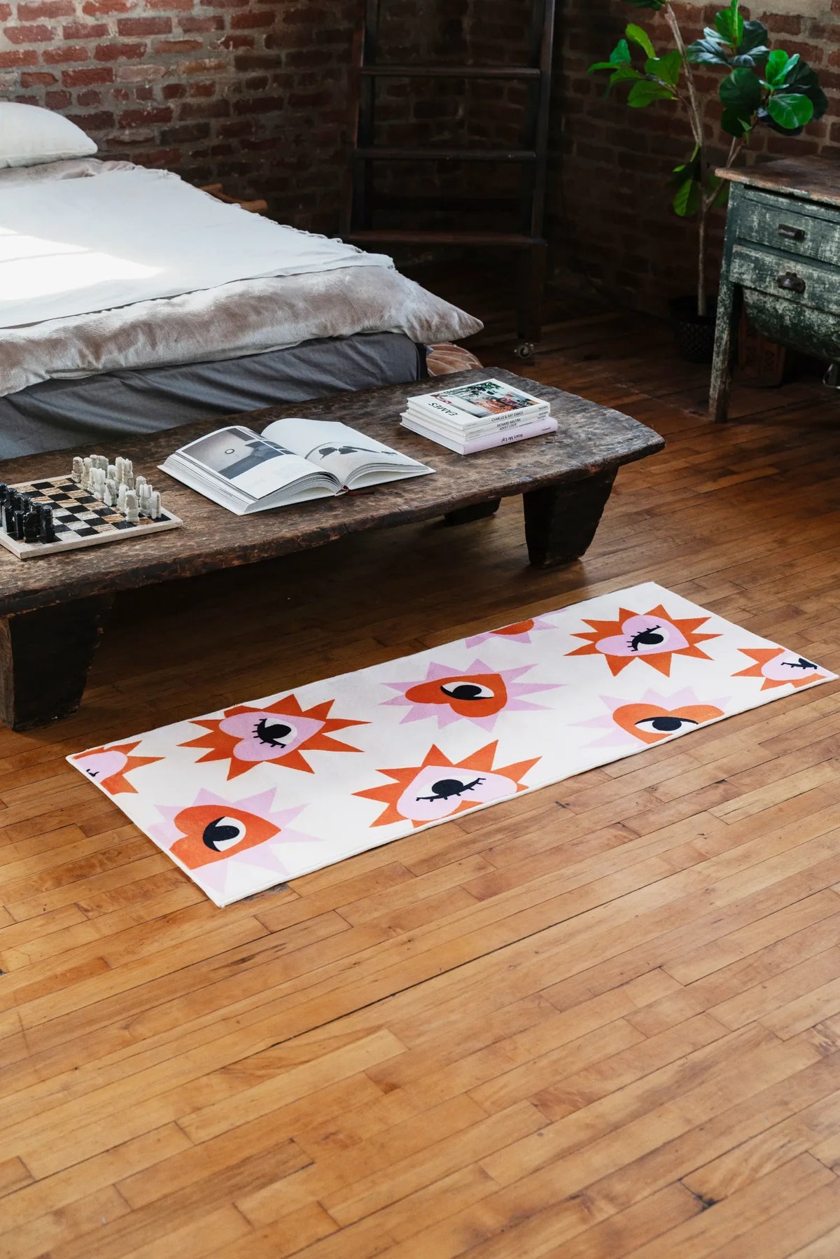 Modern area rug in heart eye design set on wooden floor at foot of rustic bench with books and plants in cozy bedroom