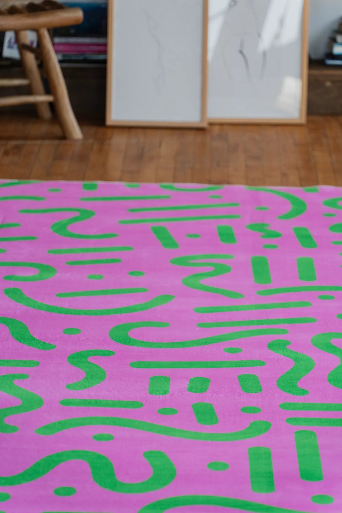 Close view of pink and green retro rug showing vivid abstract pattern spread across polished wood floor.