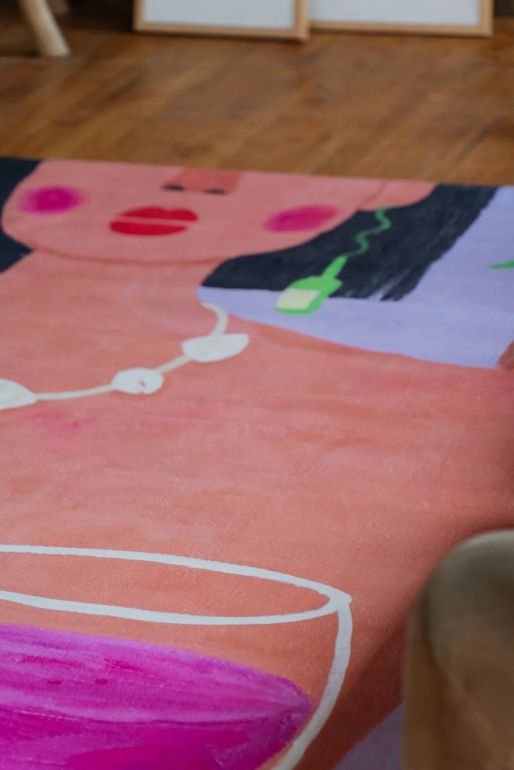 A funky art rug with vivid pink wine design placed close to sofa edge with woman face motif leading toward sketches.