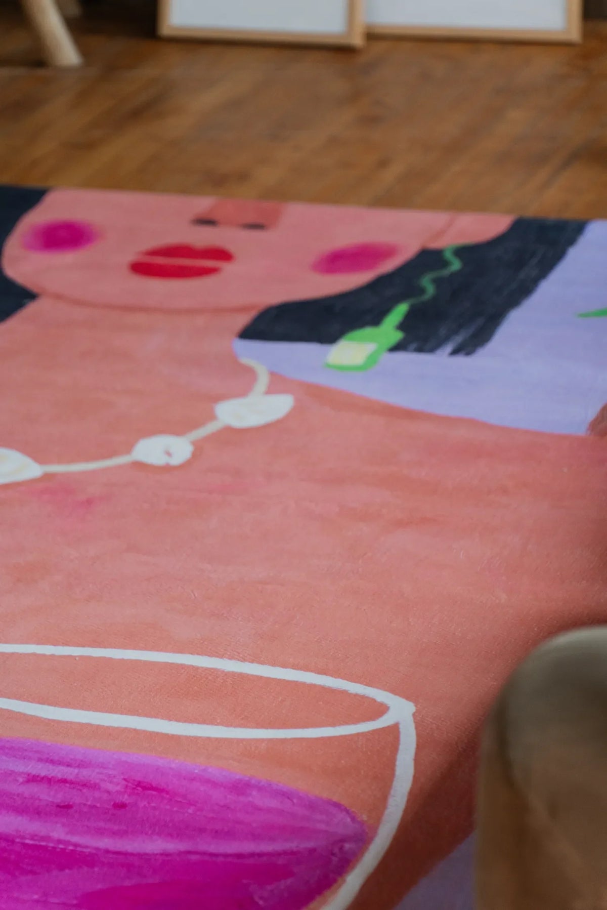 A funky art rug with vivid pink wine design placed close to sofa edge with woman face motif leading toward sketches.