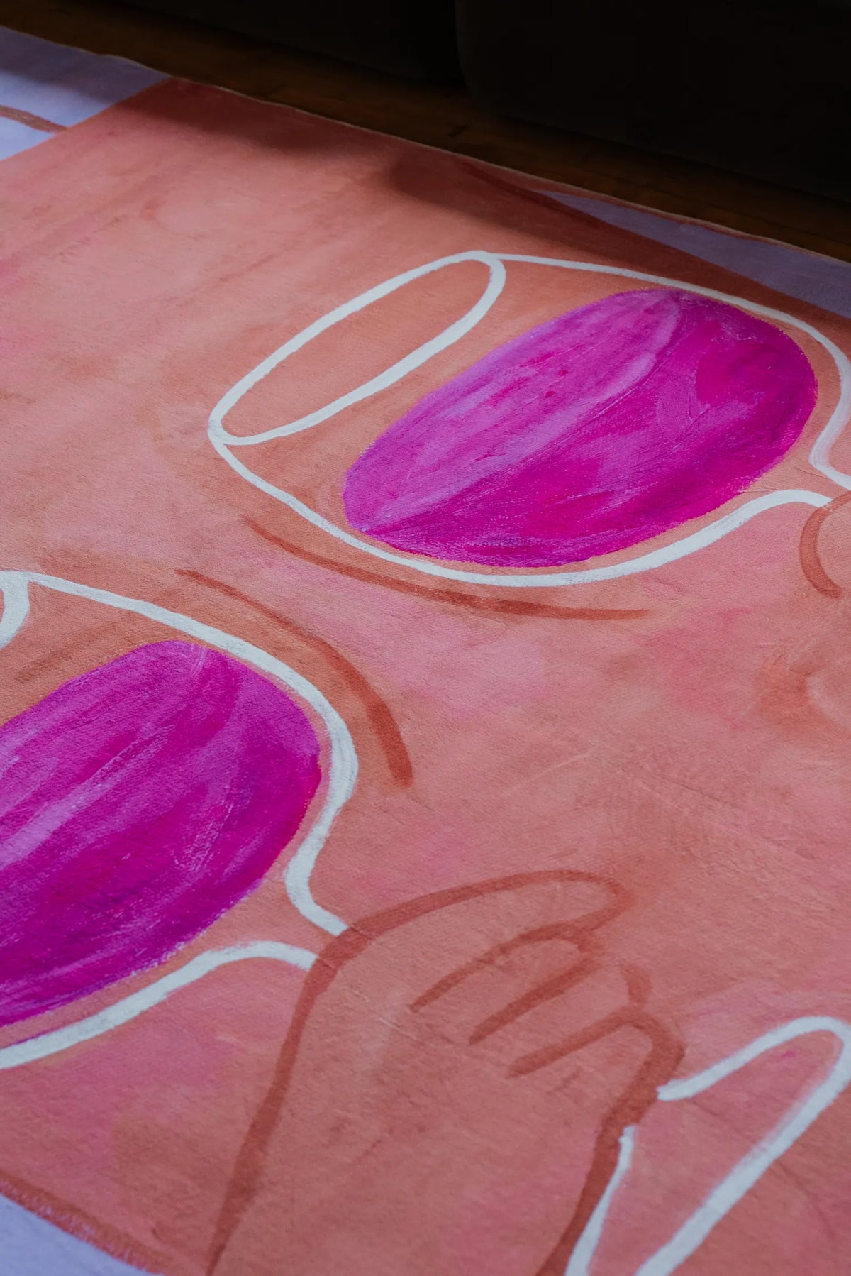 Close-up of playful rug with bright pink wine glasses on peach background placed neatly beside a dark sofa edge.