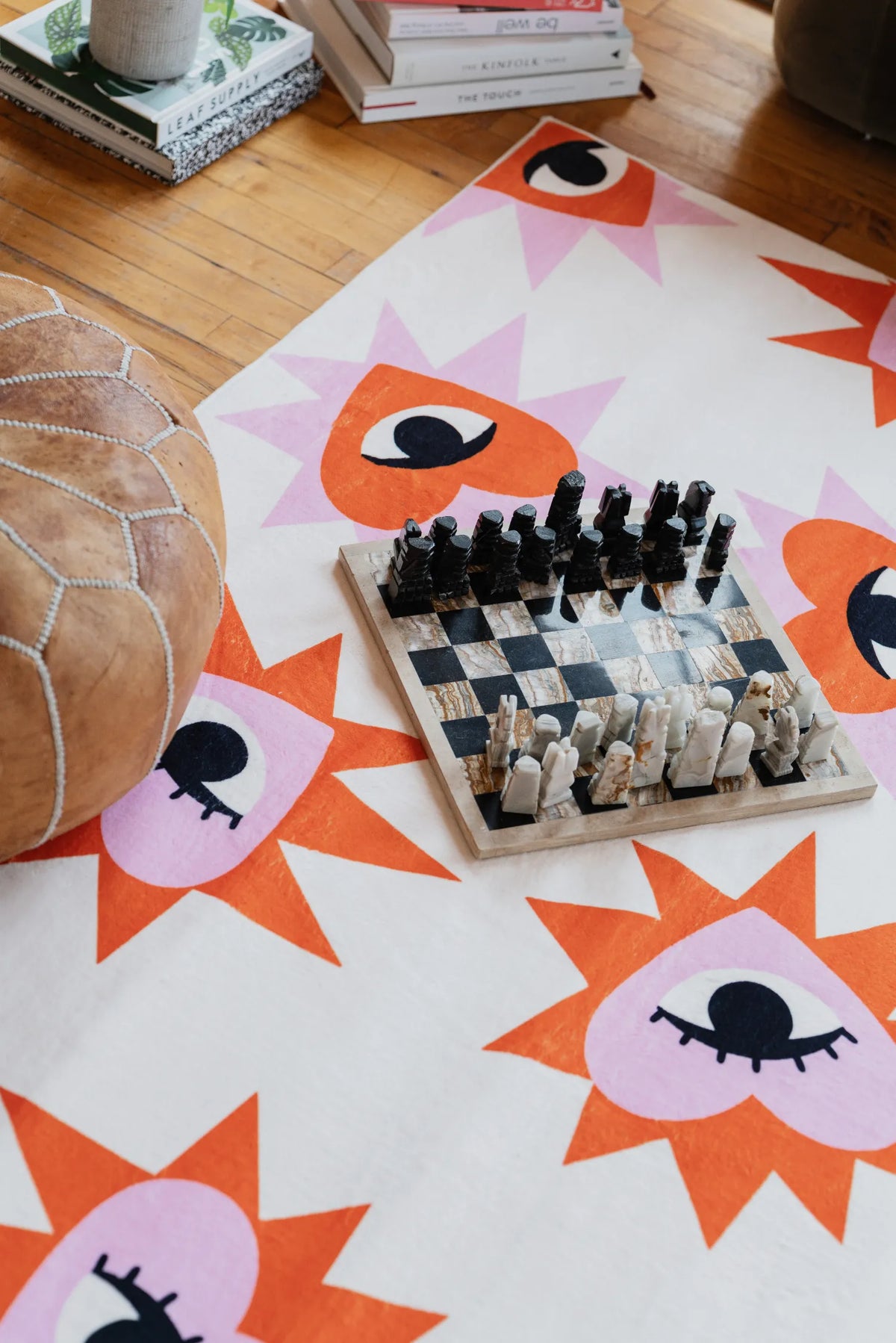 Heart Eye Pattern Rug by Megan Roy styled with a chessboard and pouf on wood floor and adding playful charm to the living room