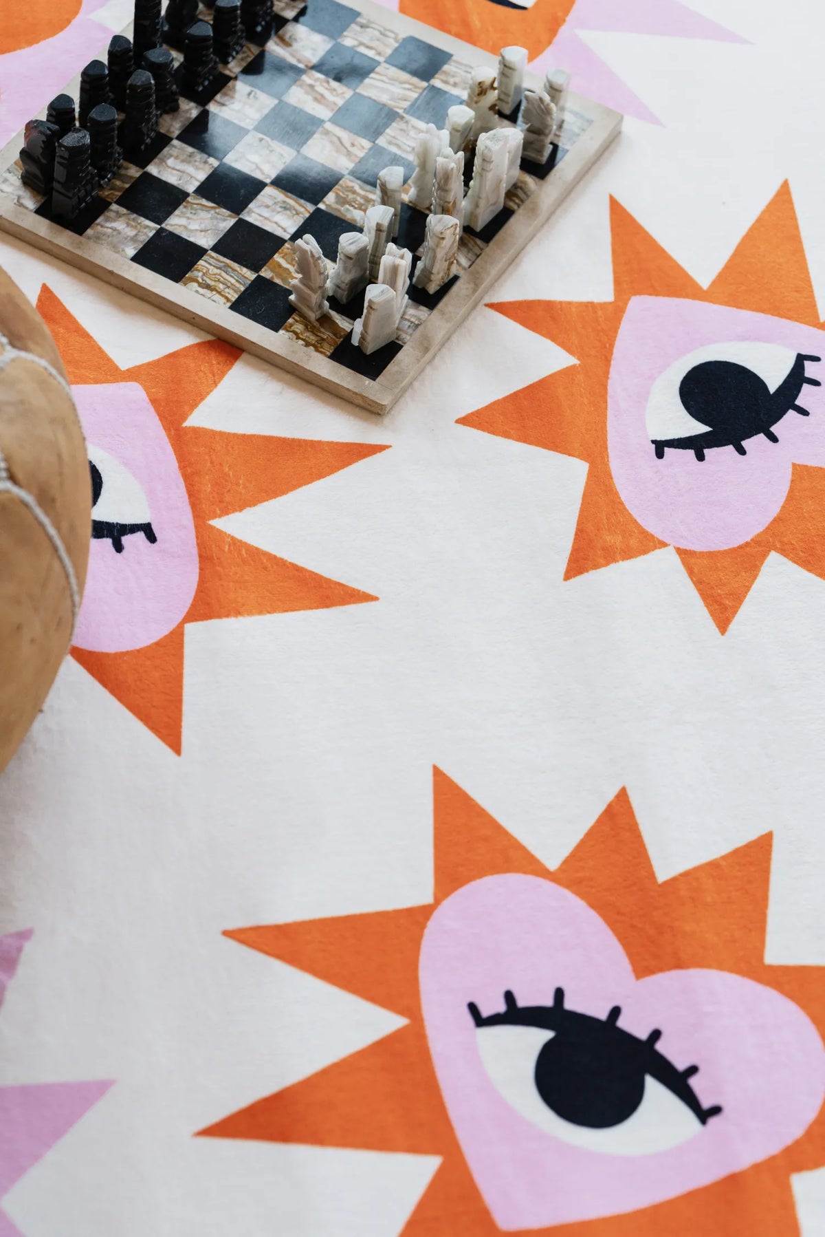 Close view of heart eye rug with bright patterns and a chess set and pouf on wooden floor and creating a bold accent in the cozy corner