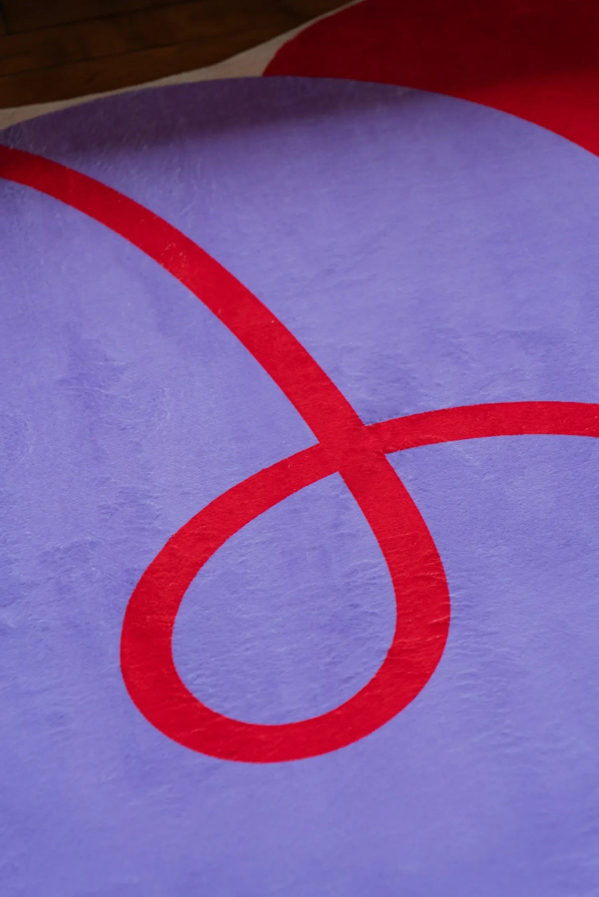 Detail of the rug’s red swirl pattern on the lilac surface, highlighting the plush texture and bold abstract design.
