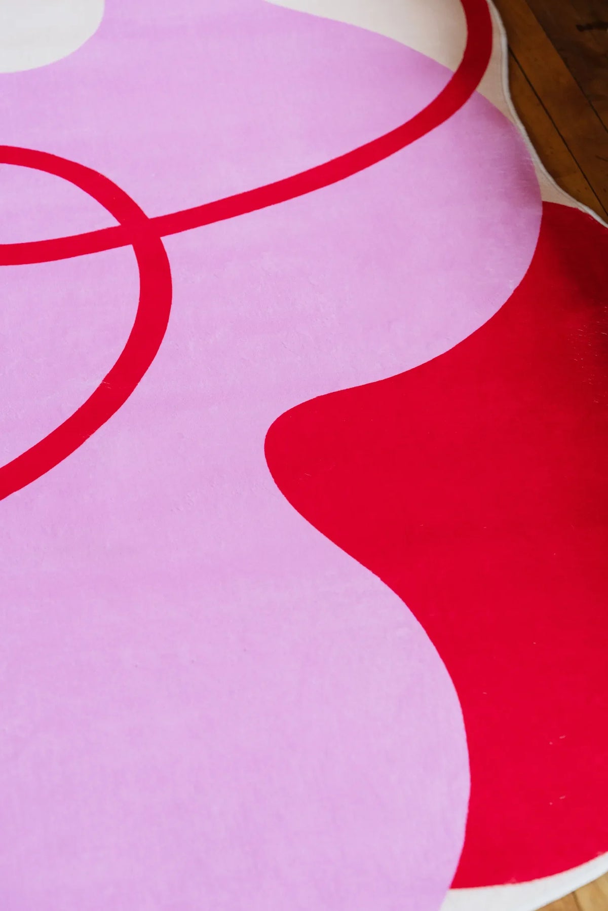Close-up view of funky pink rug with bold red curves, showing abstract texture and playful design on wood floor.