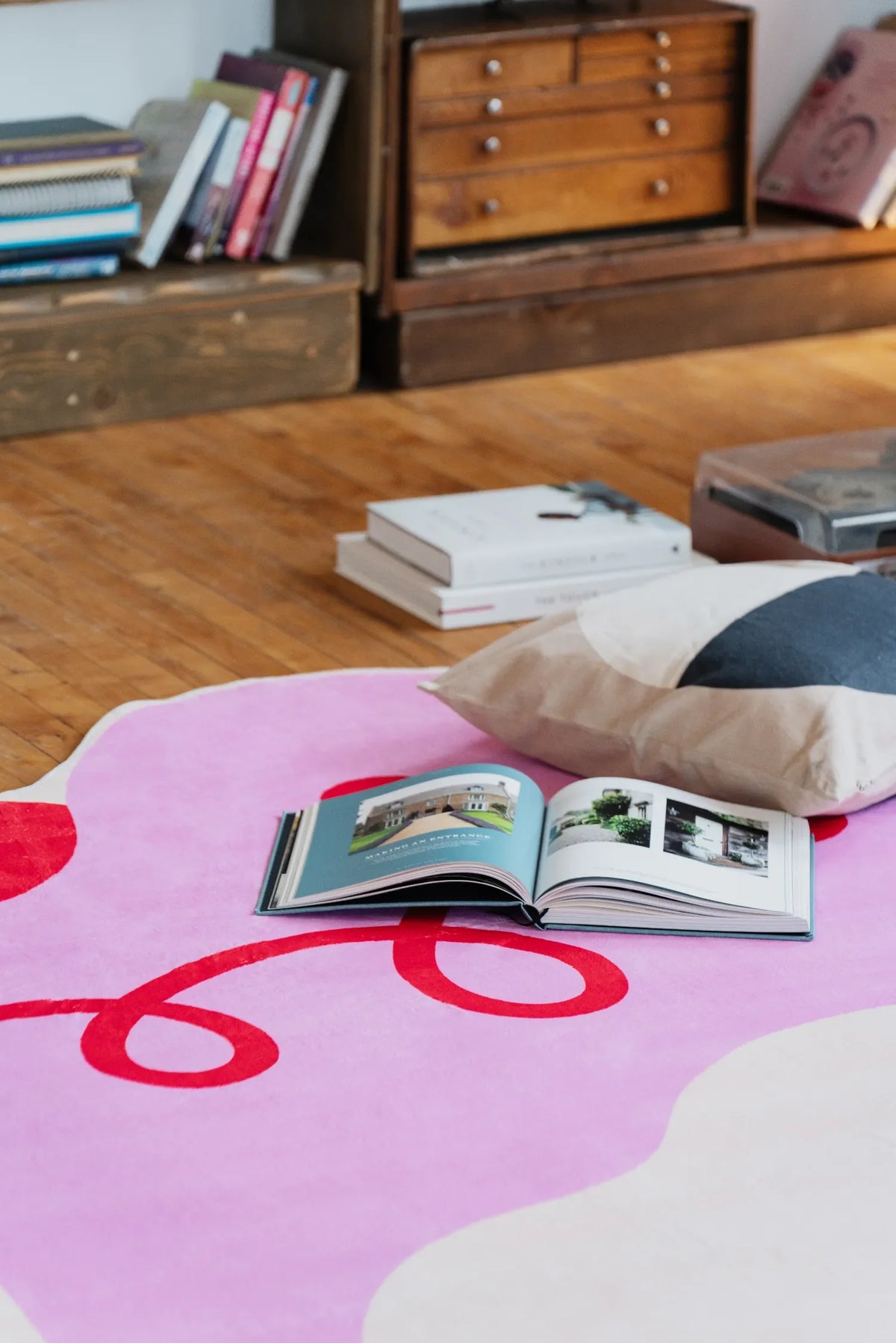 Playful pink funky rug with bold red swirls, styled with books and pillows on wood floor for a relaxed reading nook.